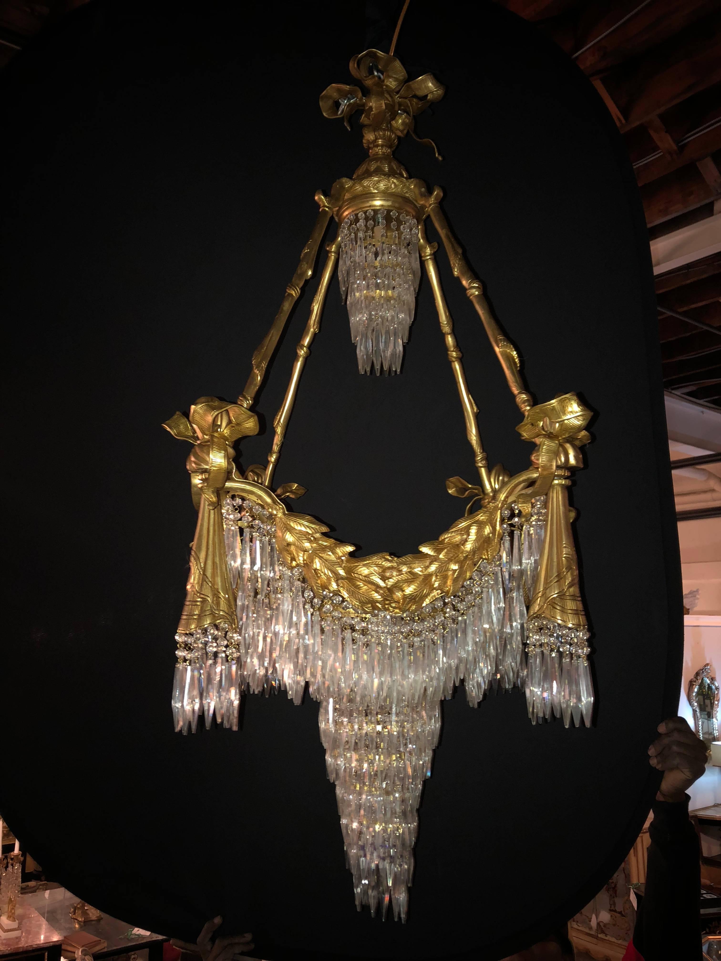 A Pair of Bronze Louis XVI style Crystal Ribbon andTassle Drapery Chandeliers with 18 lights. Each newly wired. This fine custom quality pair of chandeliers are simply stunning and are certain to light up any area of the home. The ribbon and tastle