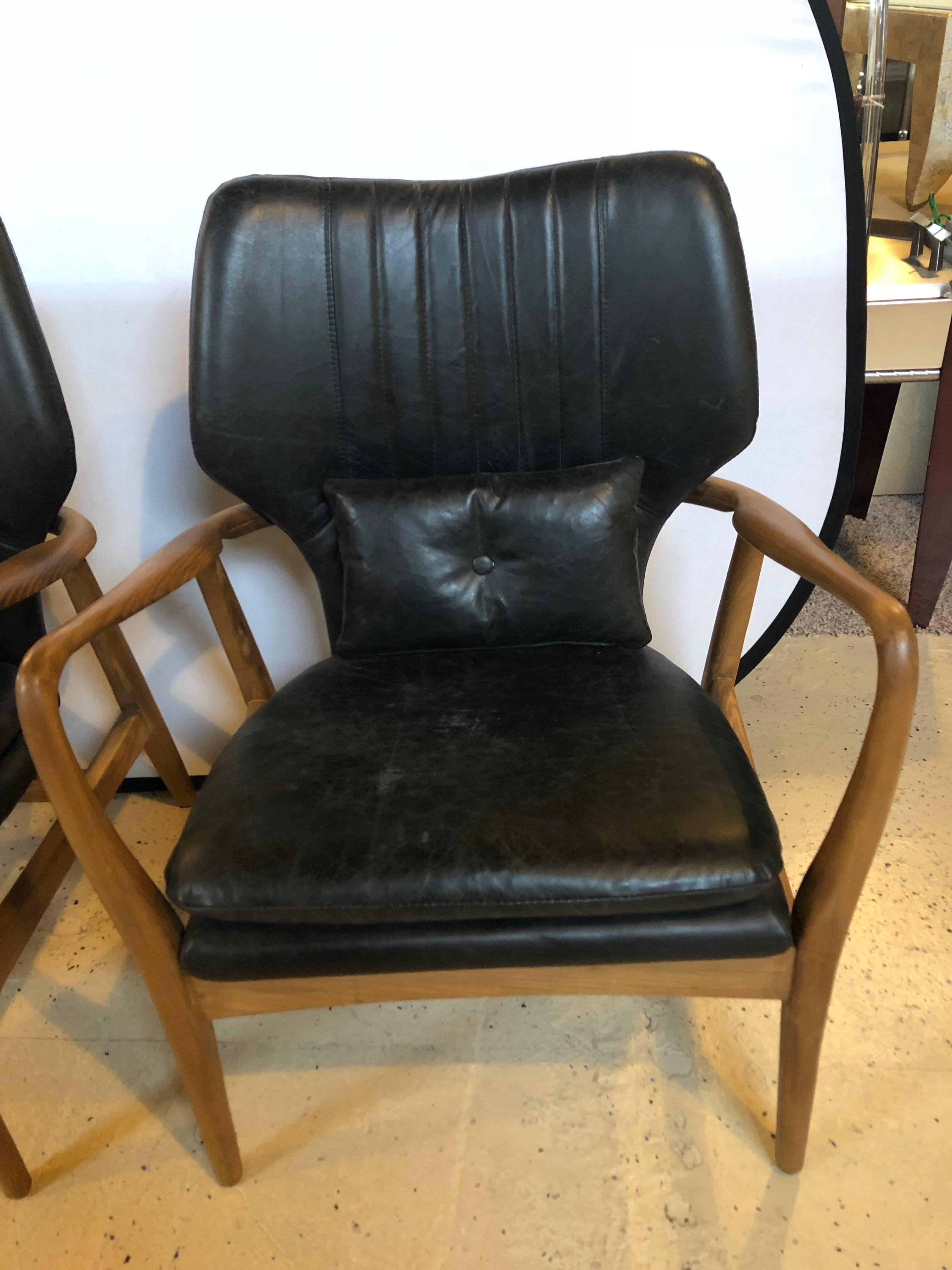 Pair of Mid-Century Modern style arm chairs with black leather upholstery. Strong and sturdy with sleek and simple lines come this finely constructed pair of arm or lounge chairs with cushion bottoms and small lower back pillows.