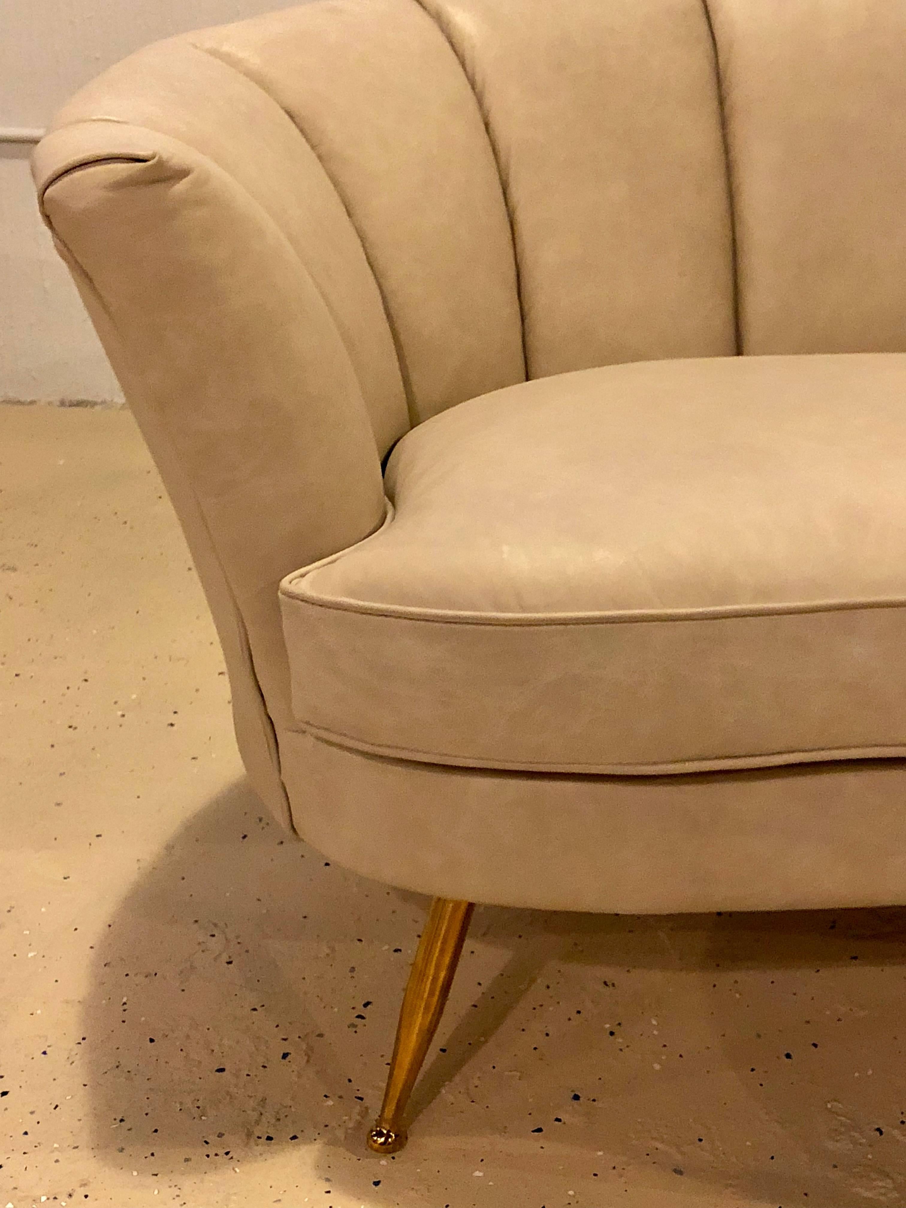 An off-white leather Mid-Century Modern settee or loveseat in the manner of Gio Ponti. A fine custom quality knockoff of this iconic designers style. The graceful and subtle lines define an era sadly gone by. The brass plated tapering legs support a