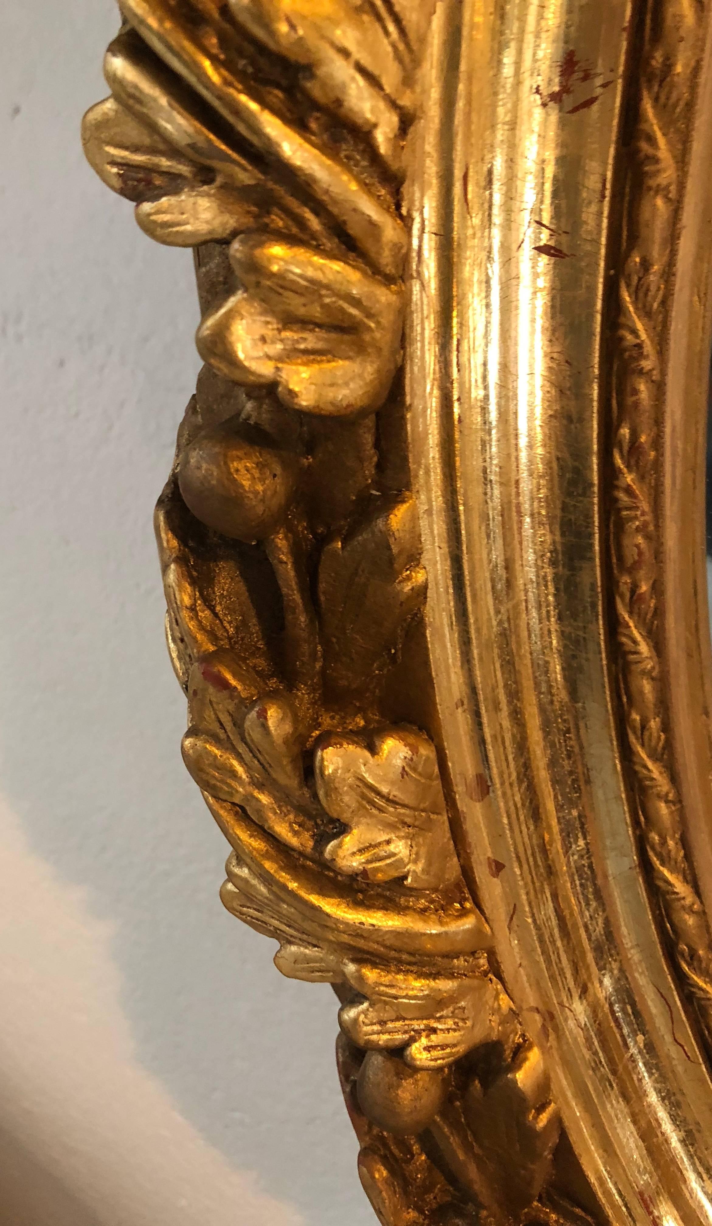 Paire de miroirs muraux ou de consoles de style Louis XVI en bois sculpté et en gesso, avec de fines sculptures de rubans et de glands. Chacun possède un miroir ovale à biseau d'un pouce dans un cadre finement sculpté de roses, de rubans et de