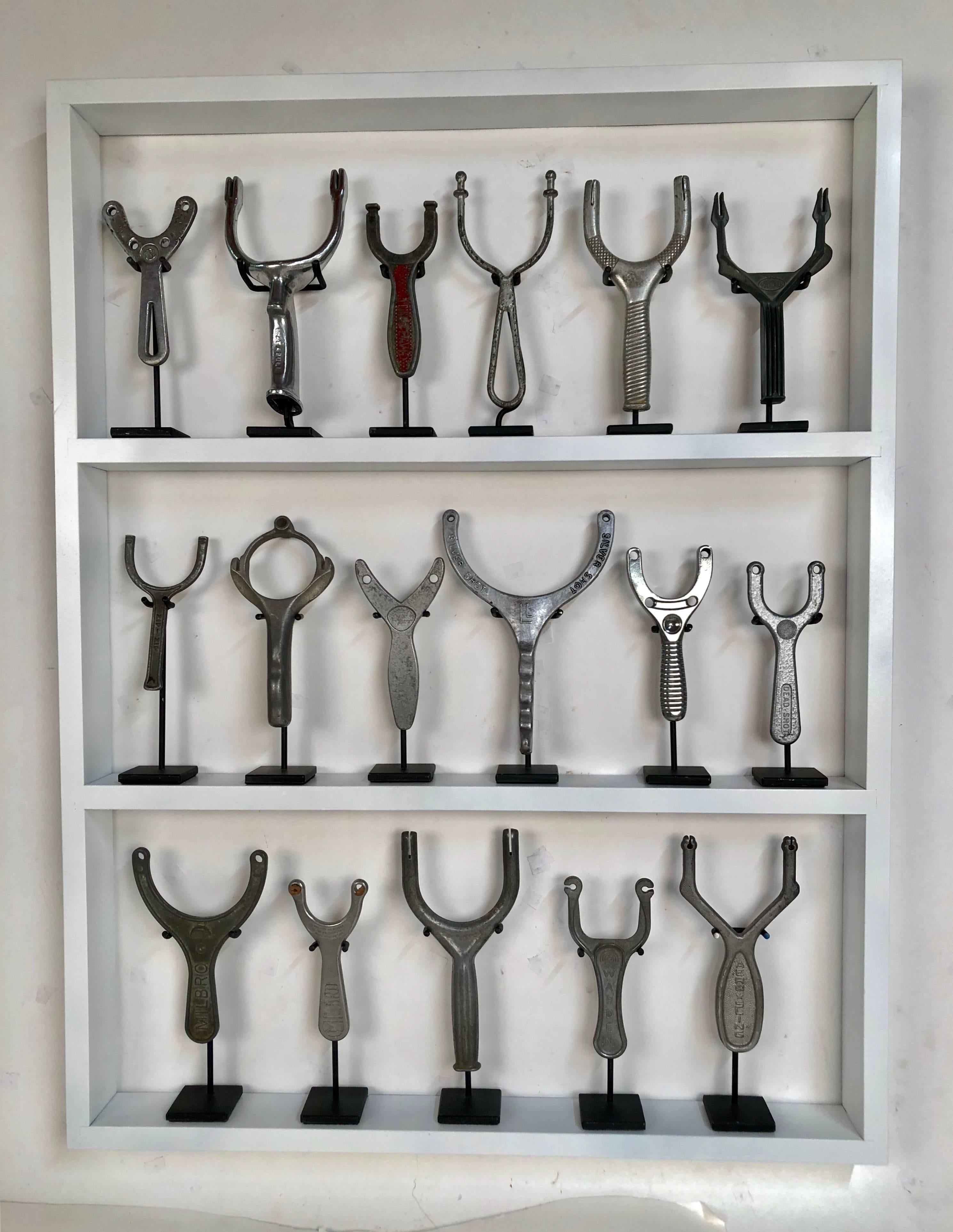 Collection of 17 unusual aluminium antique sling shots in a custom shadow box frame. These unique sling shots are all on individual custom stands. Sizes range from 7 to 9 inches in height.
