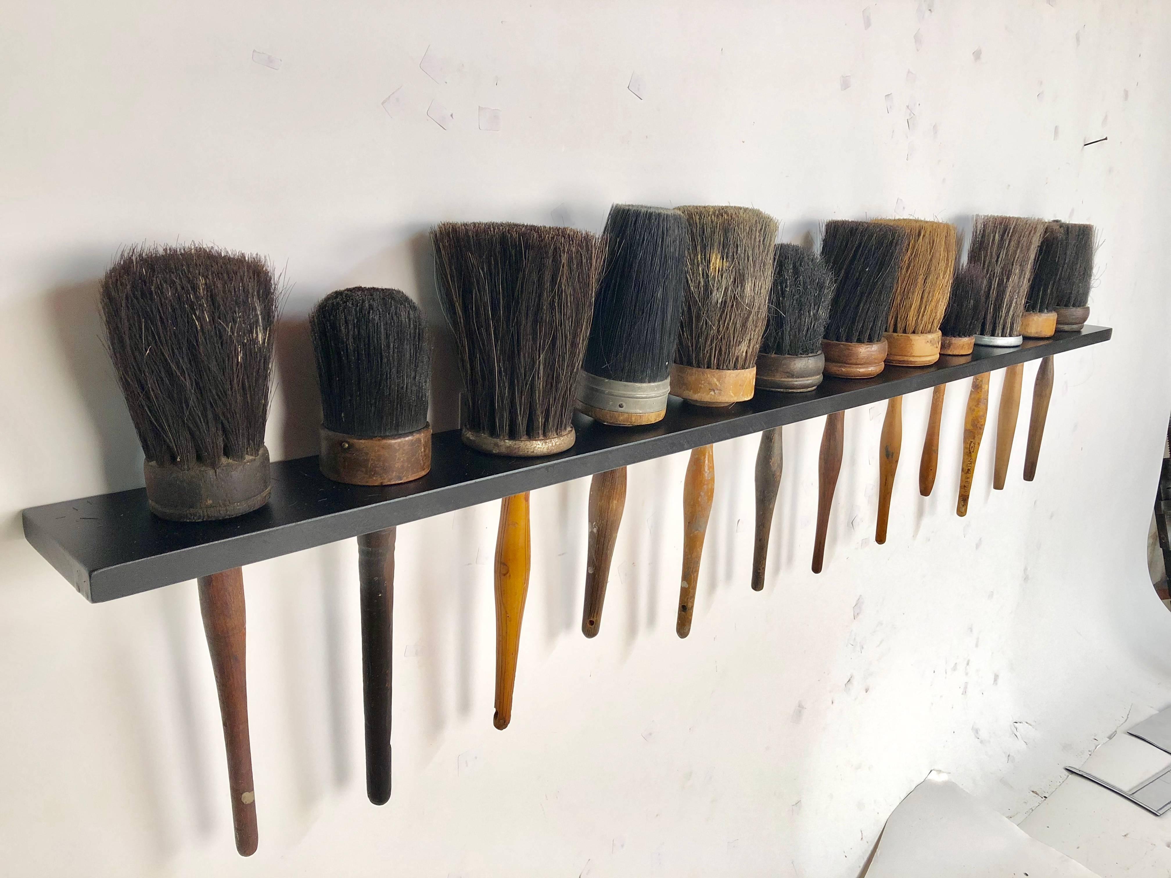 Collection of 12 antique shaker style turned wood handle horse hair brushes mounted in a custom-made black painted oak rack measuring 43 inches wide. The brushes average 13 inches long.