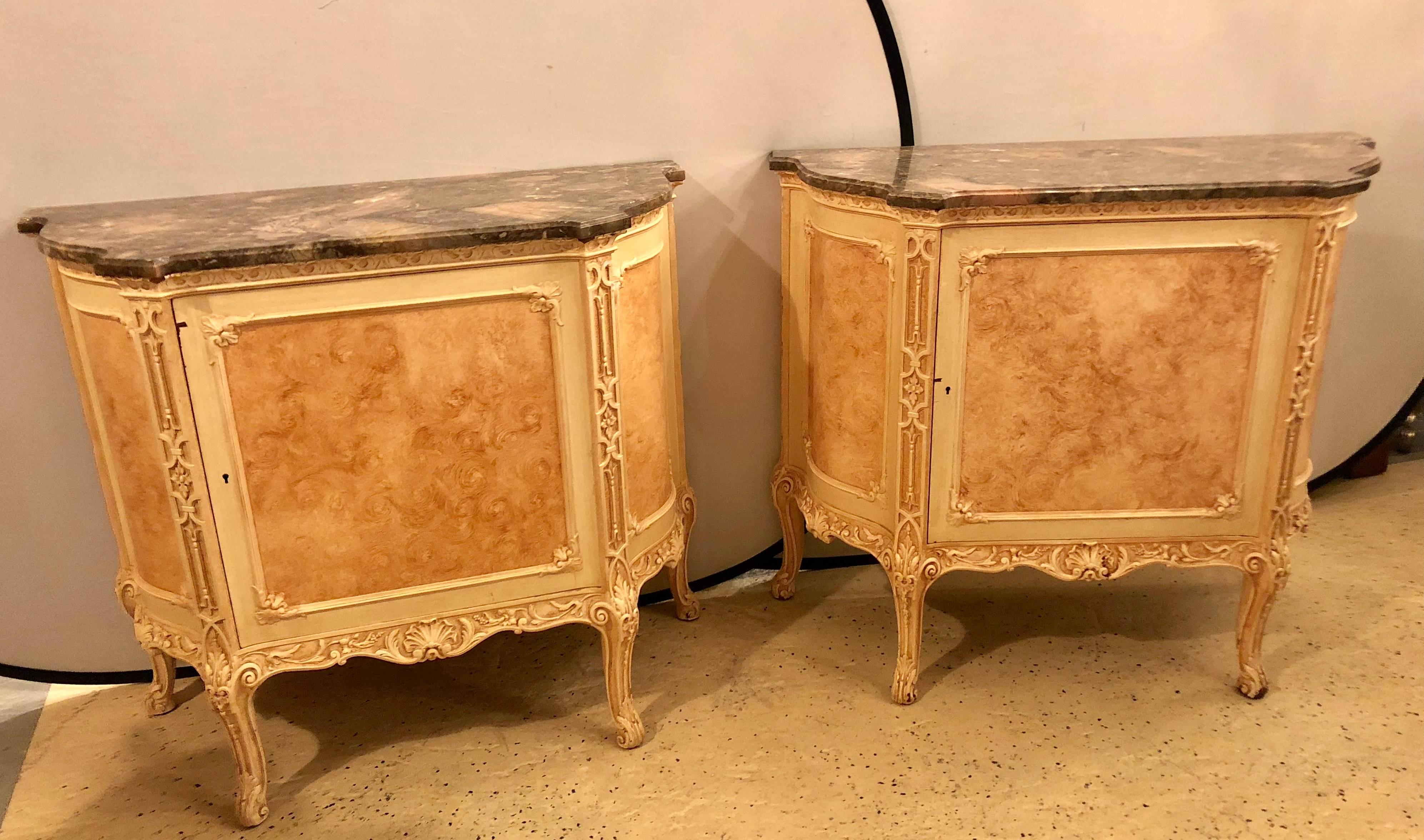 A pair of Hollywood Regency labeled 'Hostetler' faux painted Louis XV style cabinets or chests. Each having shaped custom quality marble tops over a single paneled door flanked by serpentine sides w fitted shelf interiors. All raised on carved