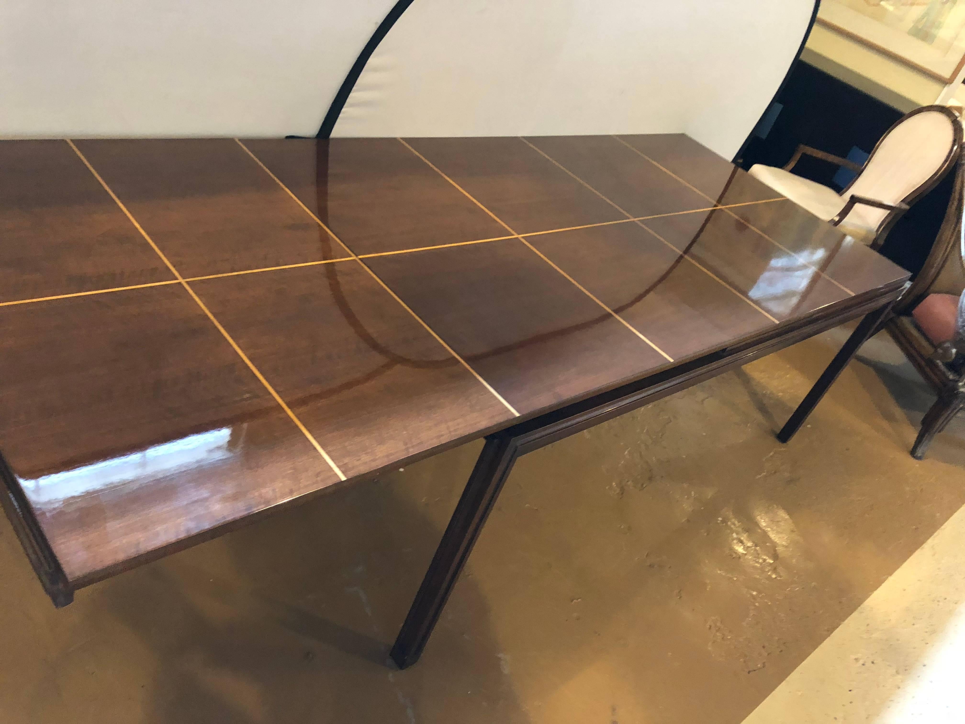 A fine Tommi Parzinger dining table having a lacquered mahogany with satinwood inlaid top. This table is wonderfully constructed by this highly sought after designer and can extend to three different sizes when one or both pull-out leaves are open.