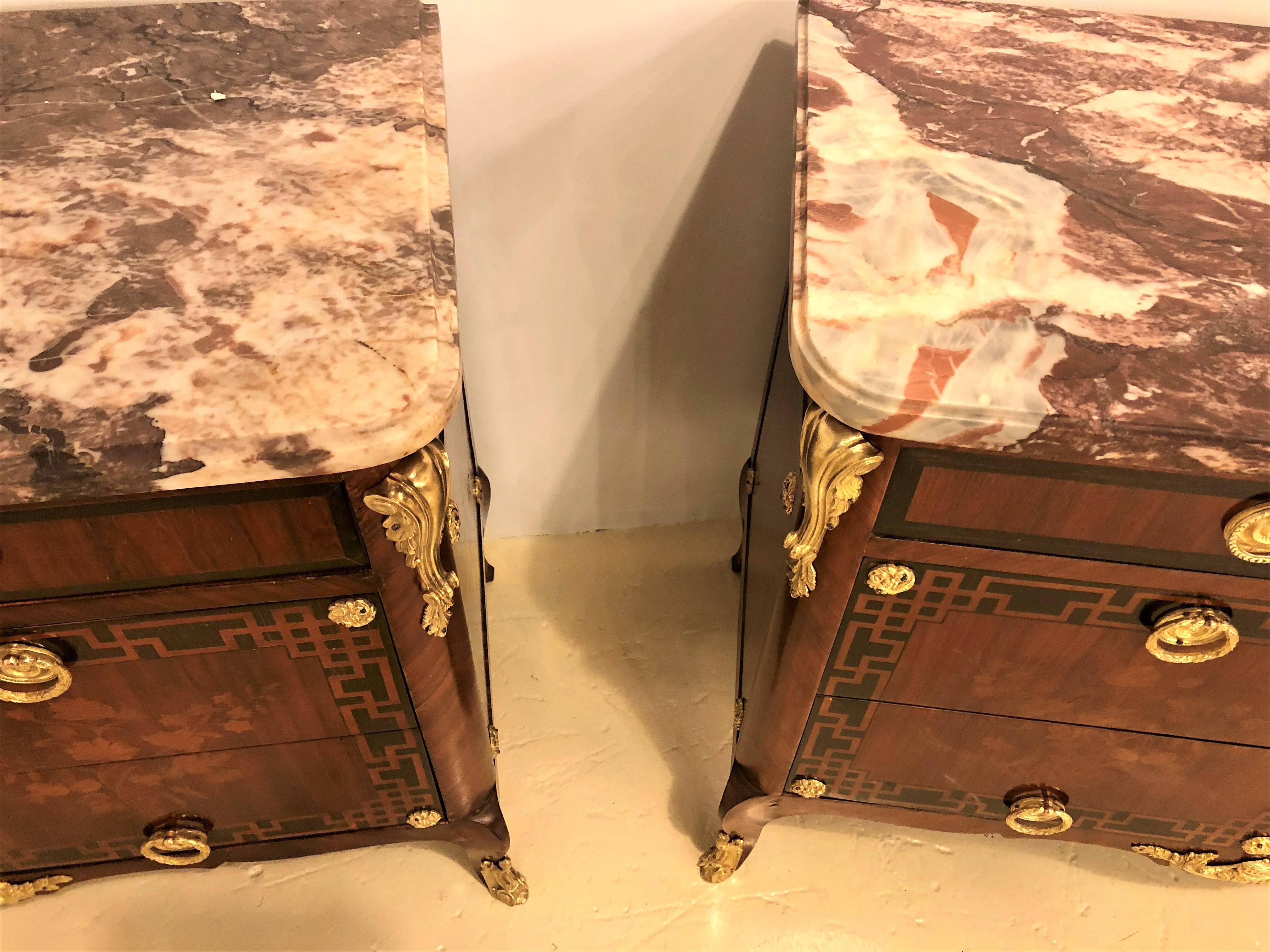 A fine pair of Louis XV style antique French floral inlaid marble-top commode or chests. The fine French marble tops of rouge and beige form supported by a group of three drawers all with ebony as well as floral inlays. The whole having bronze gilt