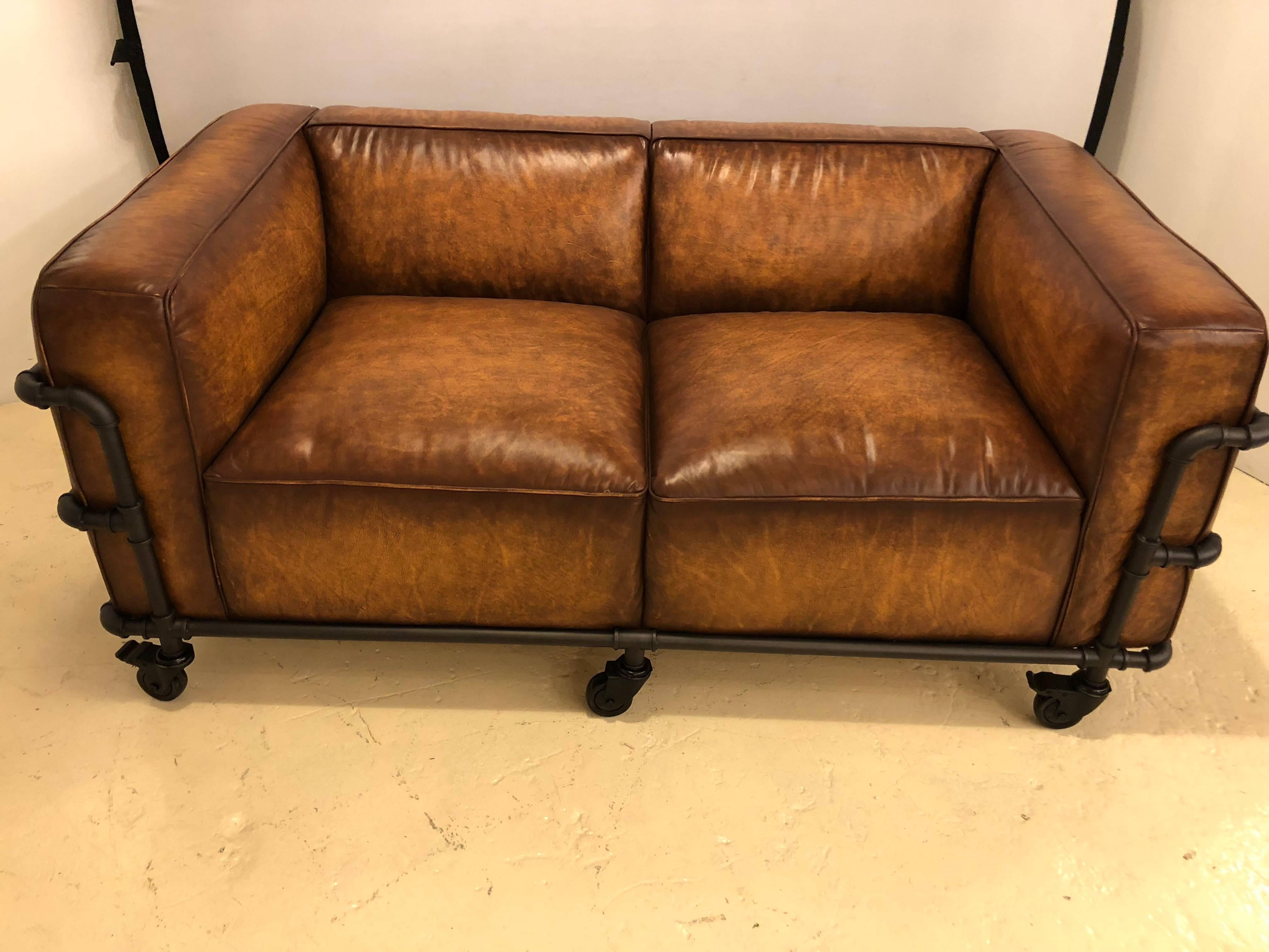 A Pair Of Industrial Framed Worn Leather Sofas  or Settees. These Loveseats each having a worn leather look  on metal pipe frames with rolling and locking casters that flow effortlessly. 