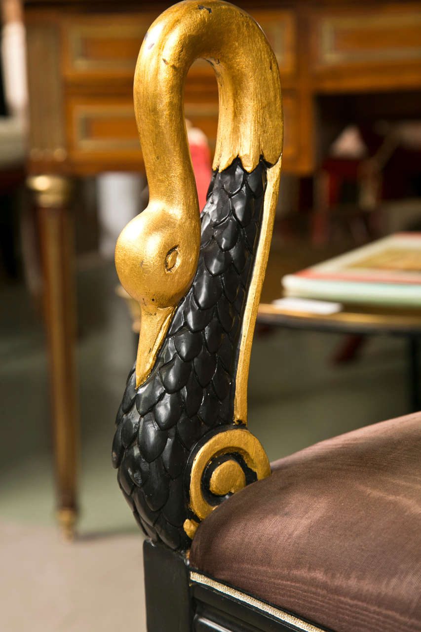 The French neoclassical taste, circa 1940s, each ebonized and parcel-gilt, the brown suede upholstered seat decorated with swan-head posts, raised on cabriole legs. By Jansen.