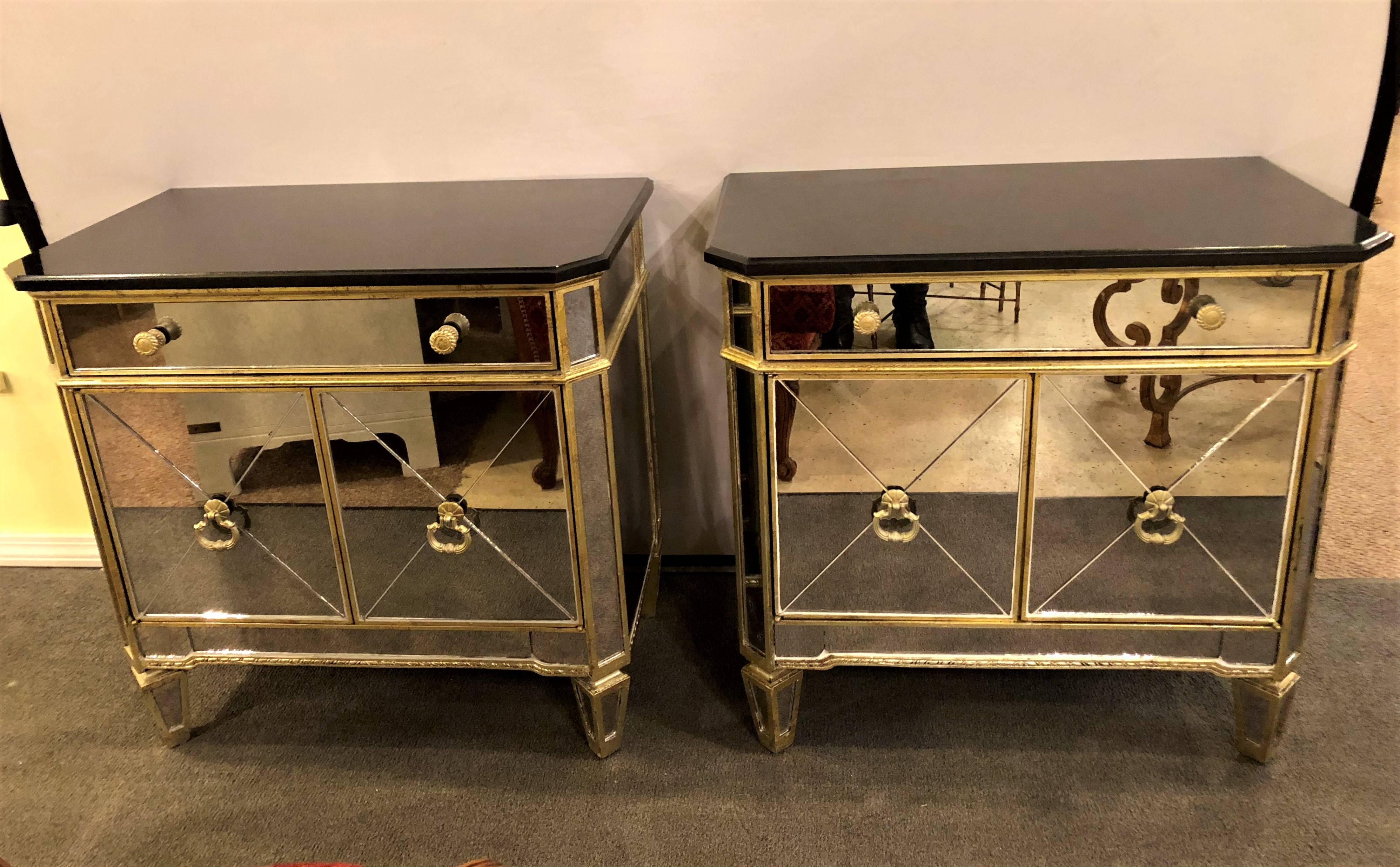 A pair of mirrored marble-top nightstands or end tables. Double doors leading into a shelved interior under a single drawer. Each having silver plated metal pulls with the casing supporting a black granite or marble top.