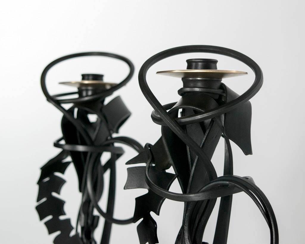 Contemporary American metal sculptor Albert Paley's pair of double shear candleholders are made of formed and fabricated blackened steel and bronze bobeches. All the candleholders in each series are stamped, dated and numbered on the base.