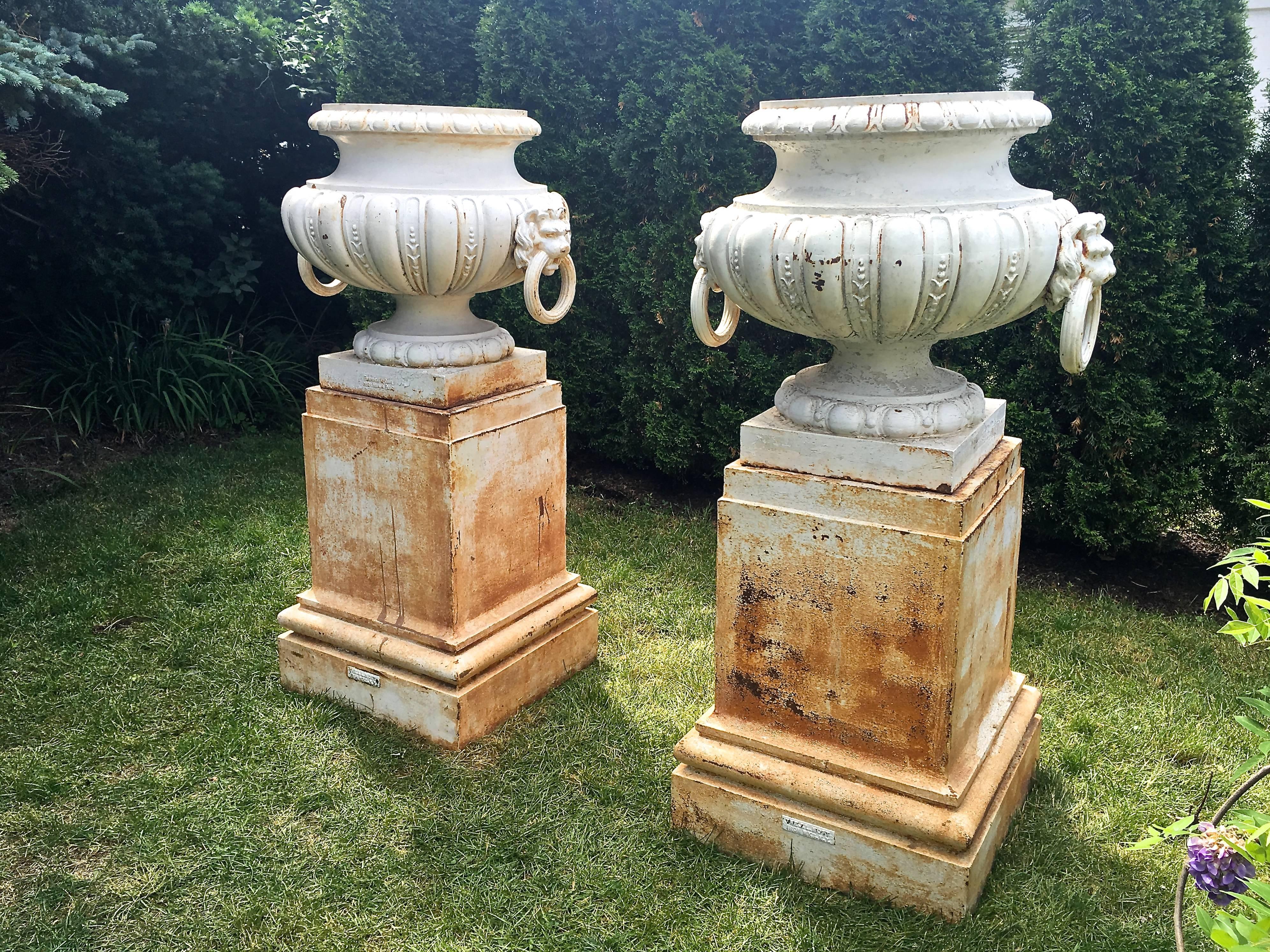 These are an exceptional and very rare pair of statuesque cast iron melon-form gadrooned urns with fixed lion mask ring handles, signed on their bases 