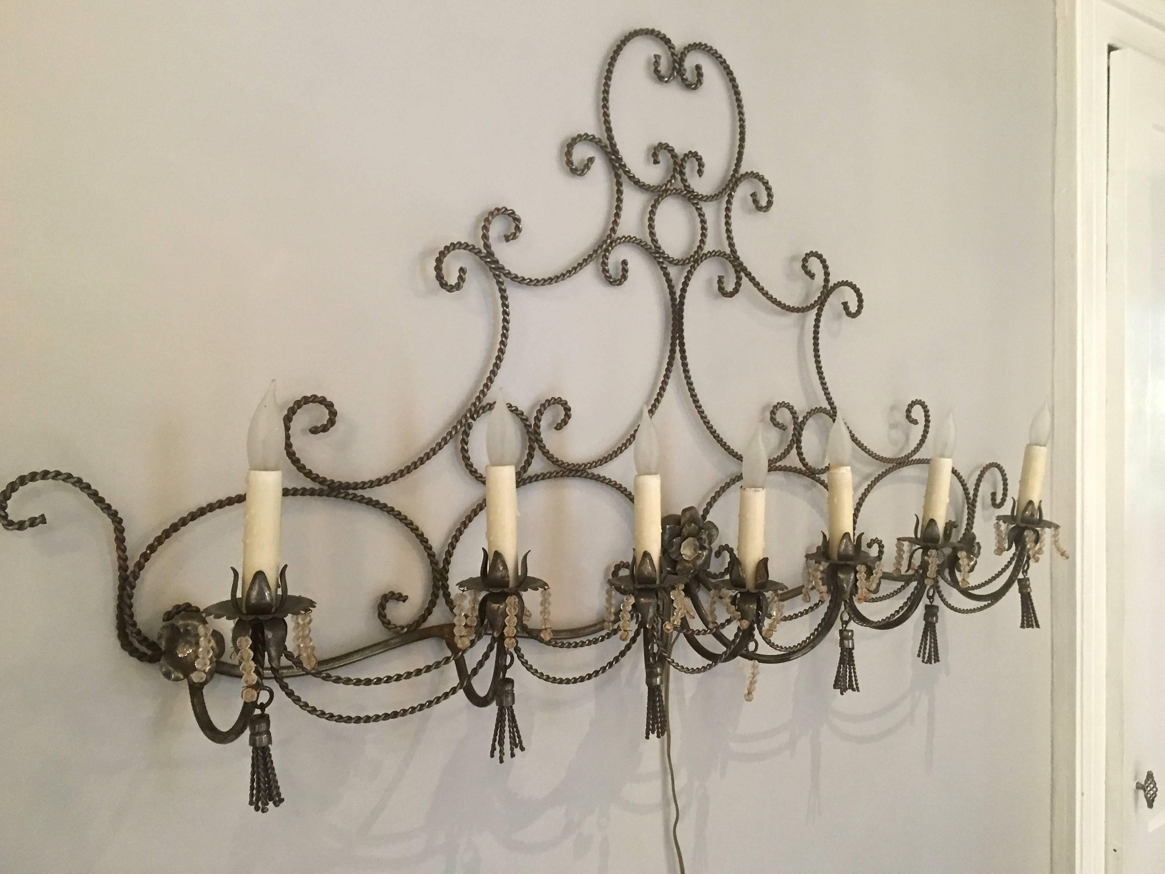 This very long six-candle wall sconce would make a perfect focal point on a wall over a bed or in a bathroom. The scrolling rope frame is accented with six candle-lights with bobeches with glass bead drops and steel tassels on each light. Gorgeous,