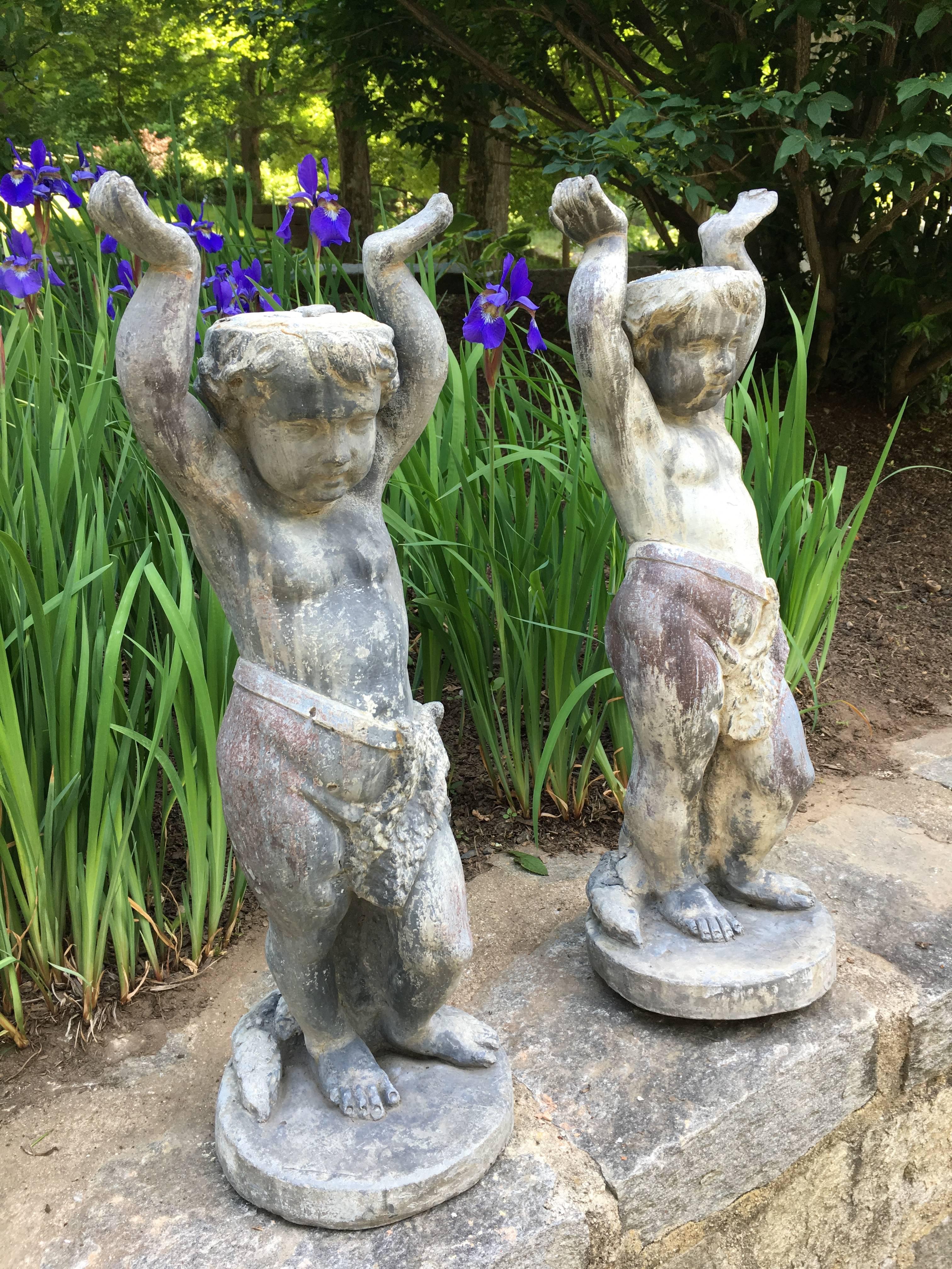 This delightful pair of cast lead putti feature upraised arms to accept either flowerpots or can serve as table bases. In lovely, weathered condition with superb patina and beautiful detail, they would make a stunning addition to either side of your