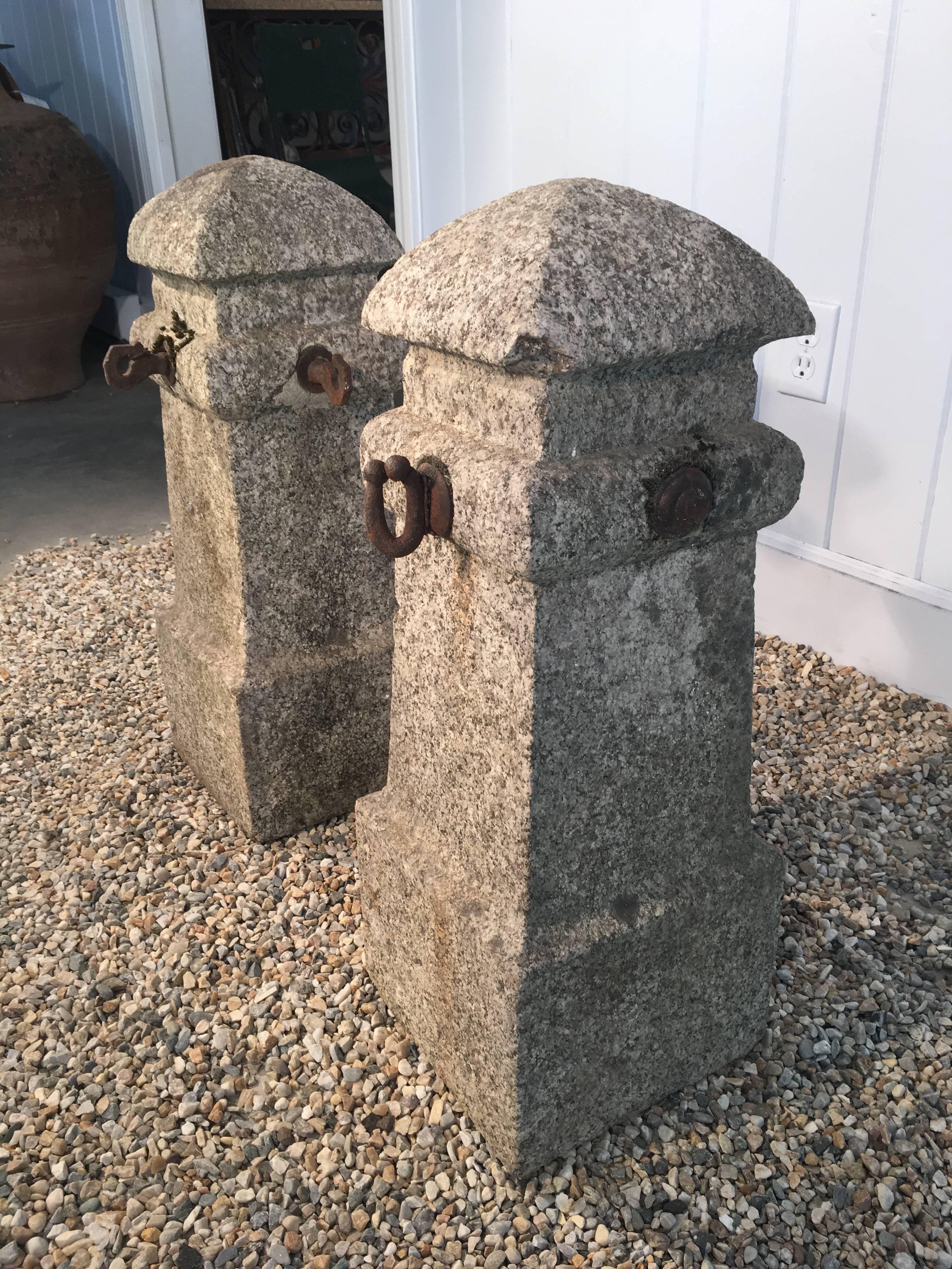 A rare pair of French granite hand-carved entrance pillars/bollards with some of original wrought iron chain anchors. One chip to one corner of each top shown in photos (well-weathered). Can be left outside all year long, regardless of climate.