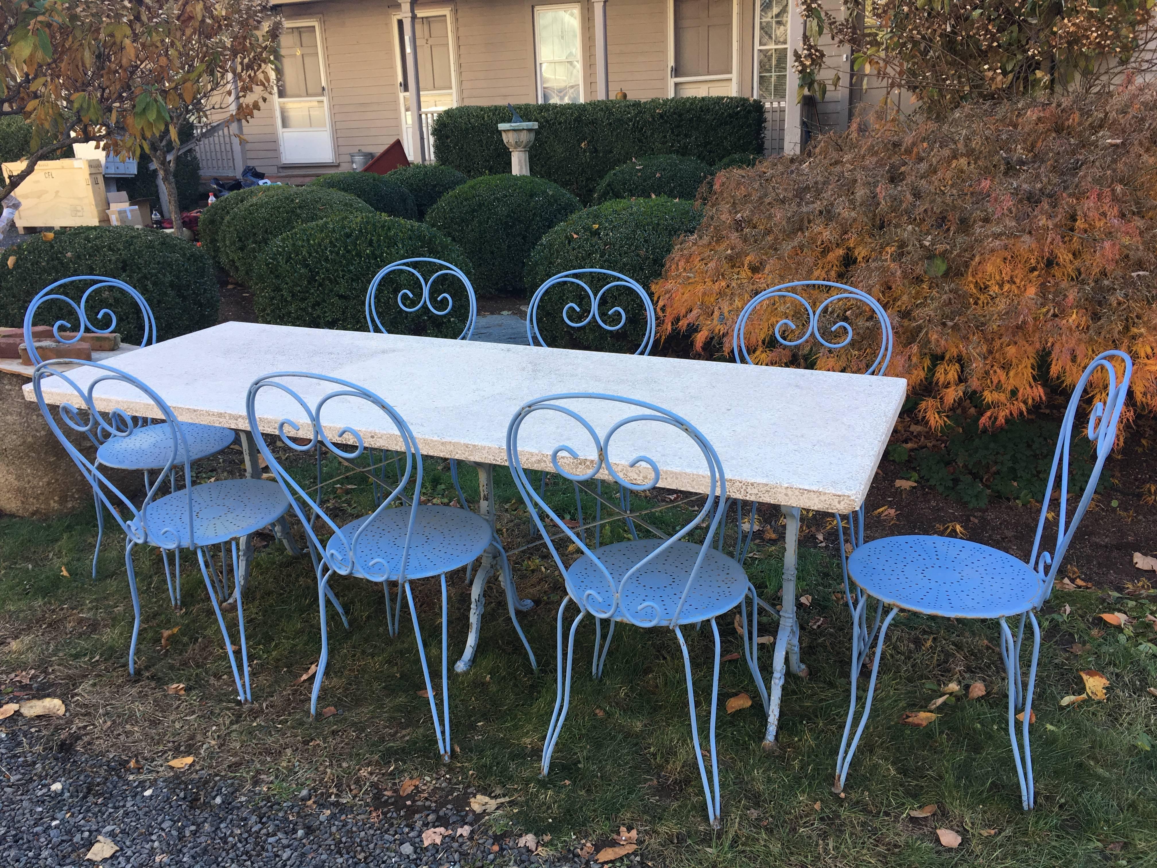 This lovely French dining set for eight comprises a triple cast iron base in old pale blue paint (signed Godin), a very heavy pale cream-colored terrazzo top, and eight classical French side chairs in faded medium blue paint. The table measures 86