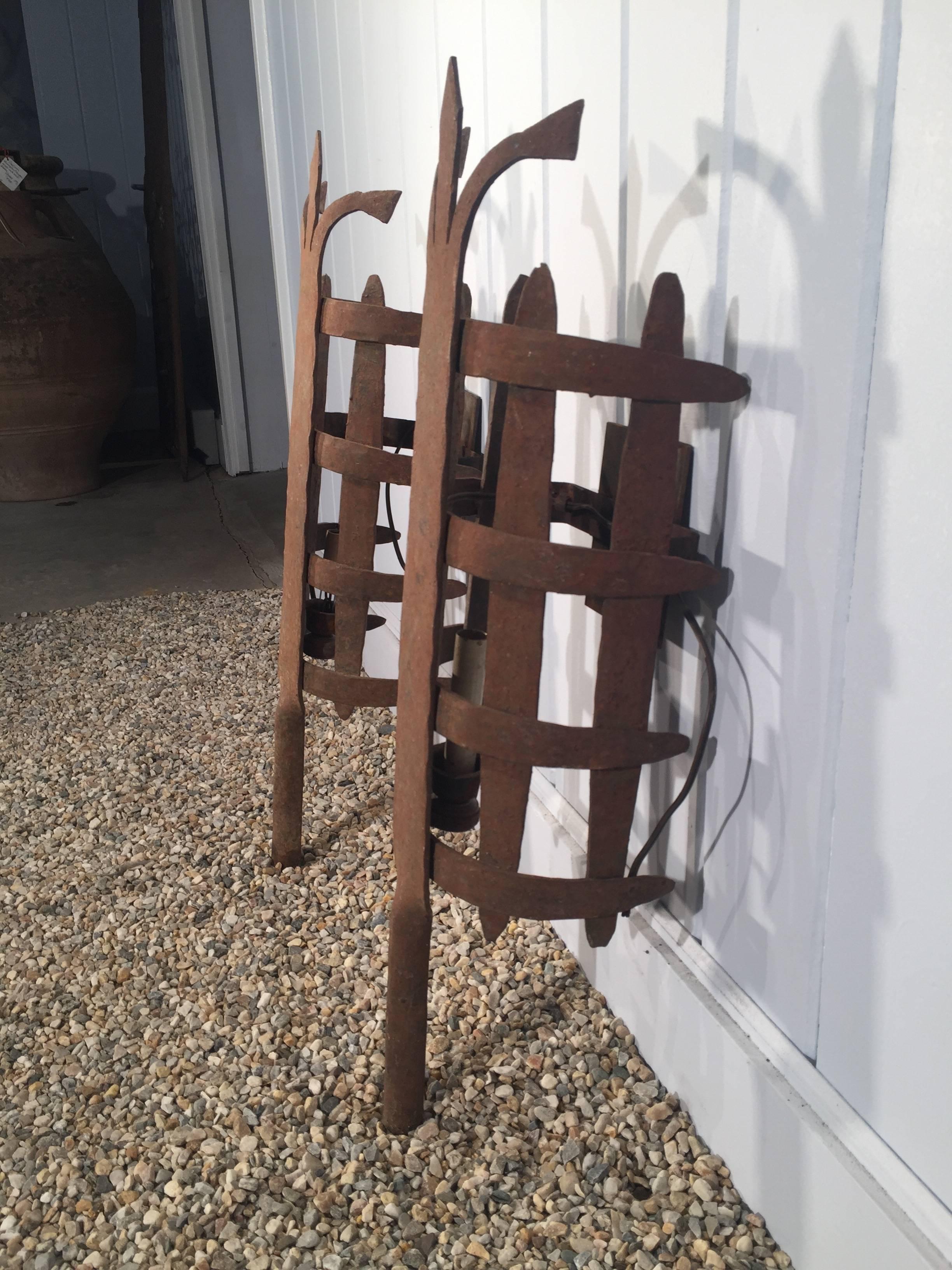 This pair of medieval curved wrought iron sconces are all made by hand and we think date to the middle of the 19th century. With a beautifully-rusted patina, we have electrified them with a single bulb socket and added steel wall plates that connect