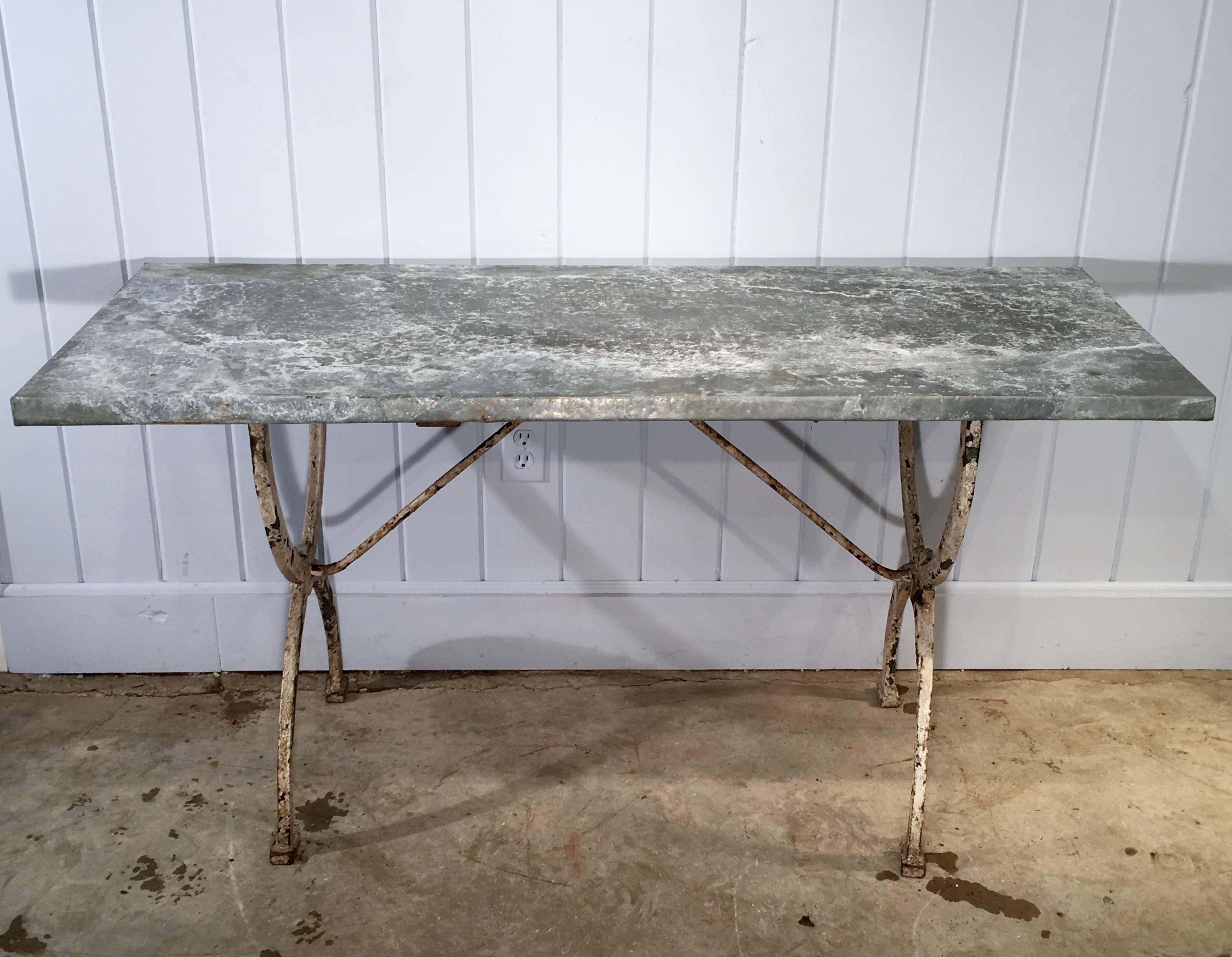 It is difficult to source old and weathered authentic zinc-topped tables, and we found two beauties, very close in size. This is the shorter of the two. Both have identical wrought-iron bases in an old creamy white painted surface with bits of