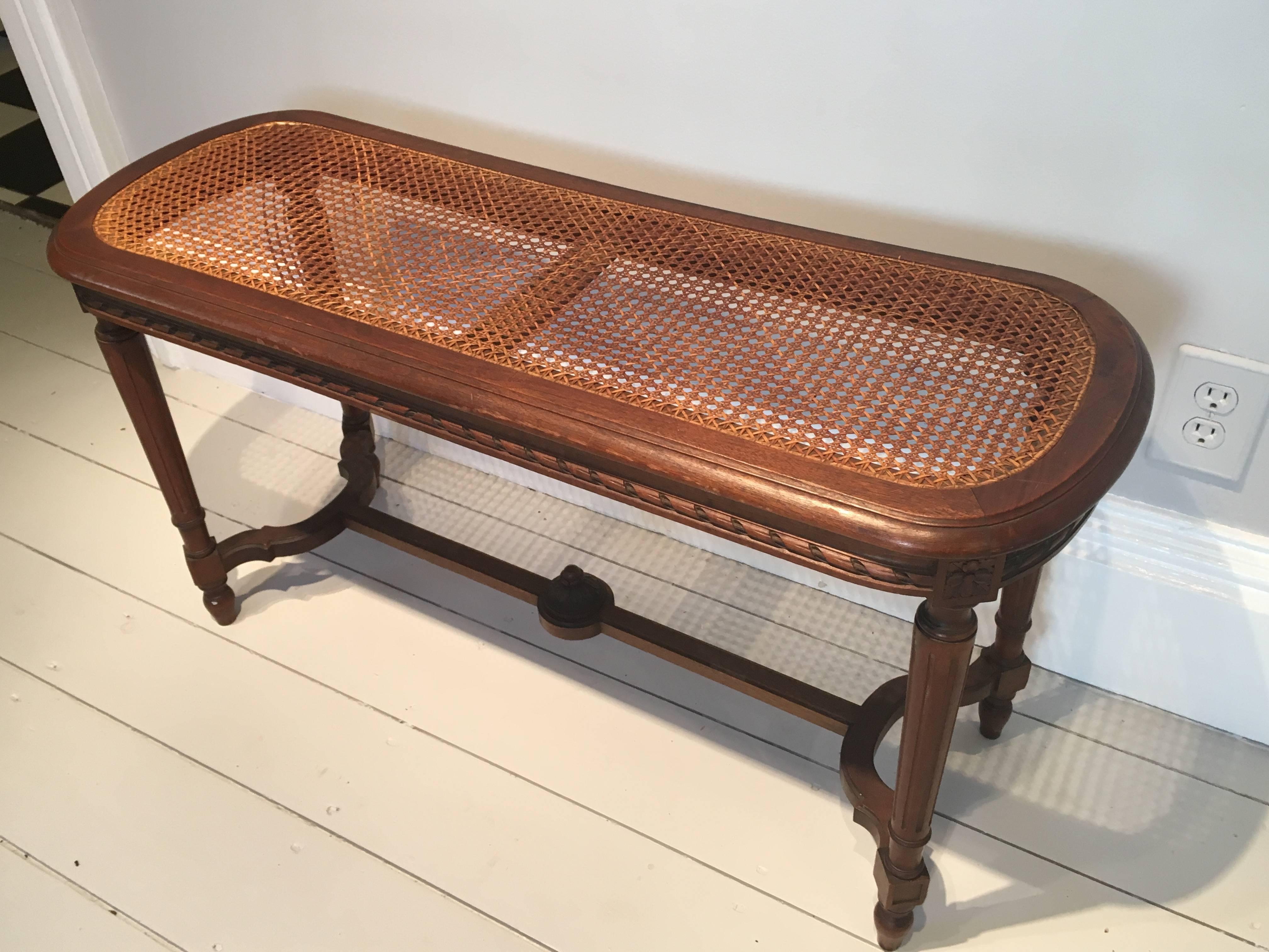 This lovely and utilitarian bench has been hand-carved from walnut with beautiful details and curved ends and side stretchers. The caning is in perfect condition and it would make a stunning addition to the end of a bed or as a coffee table. We are