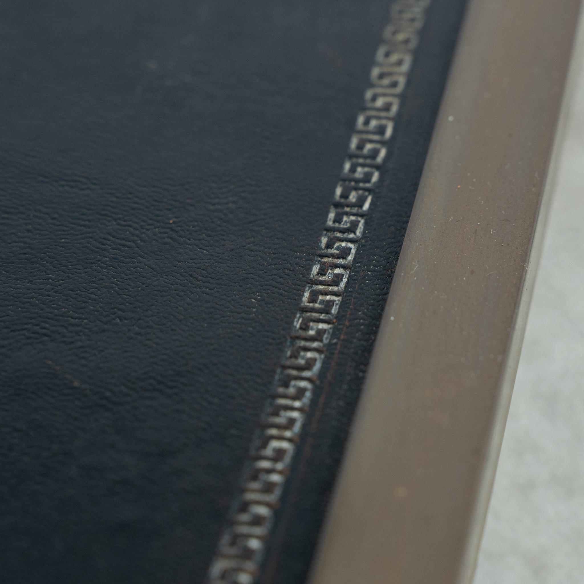 Table basse de la Maison Maison/One, avec un plateau en verre transparent et une tablette inférieure en cuir estampé noir avec un motif de clé grecque.
Il s'agit d'un modèle plus rare, avec un travail du métal très élégant, y compris des épis de