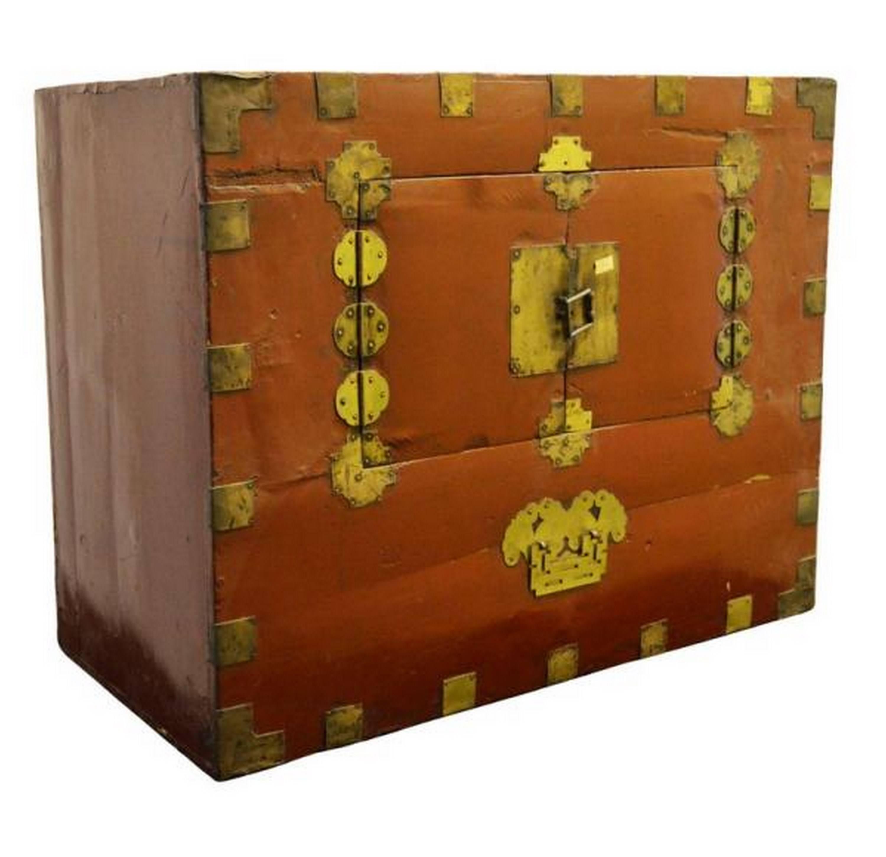 This Korean chest from the early 20th century displays a nicely varnished wood panel, adorned on its front with traditional brass hardware. The chest opens thanks to a double door with hinges that are also splendidly carved brass. Under the lock
