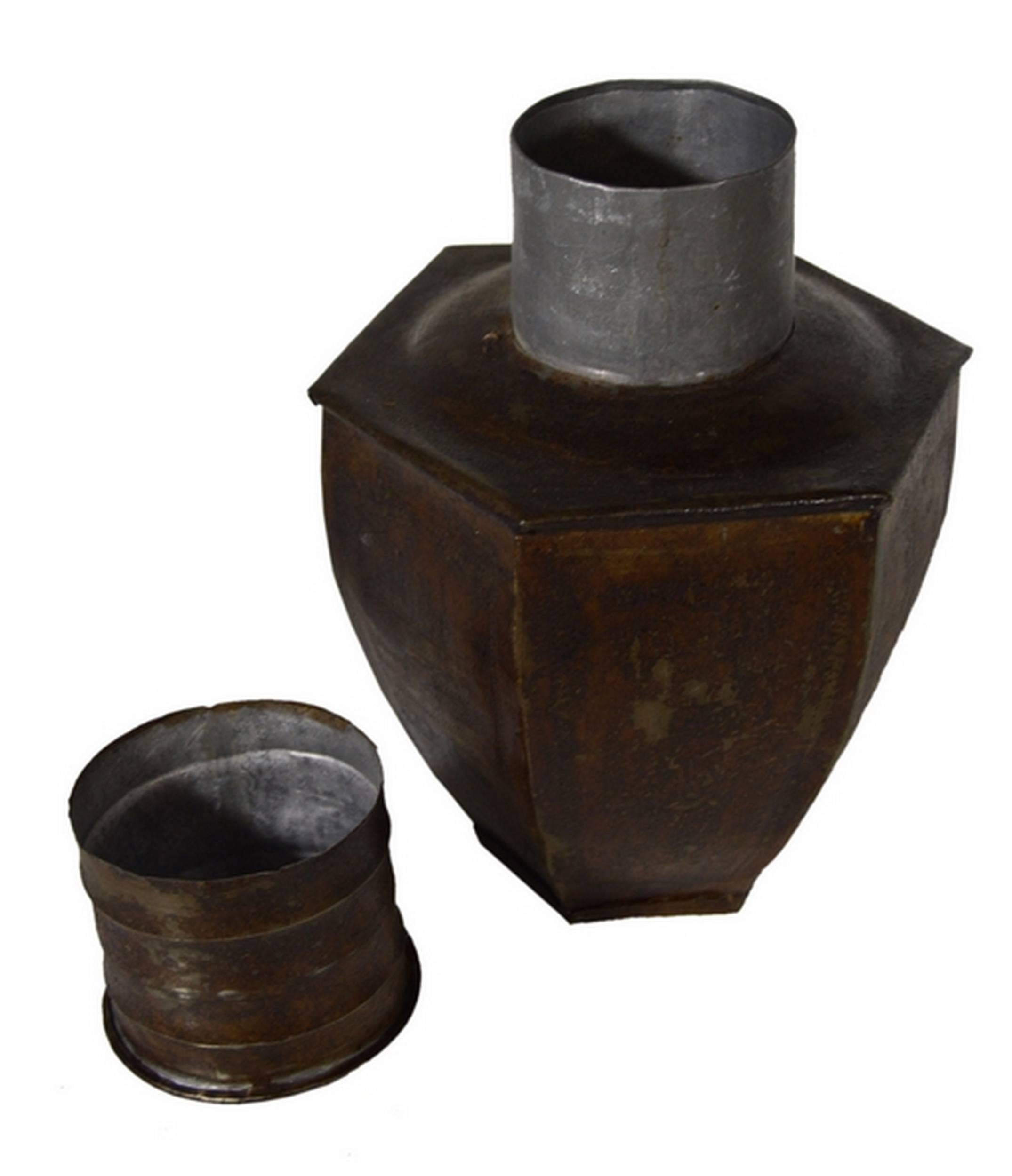 A 1930s multi-sided storage canister hand-hammered with tin in India. This canister displays a six sides shape with a narrow bottom and a large belly. The flat top features a cylindrical neck closing thanks to a striped cylindrical lid. This