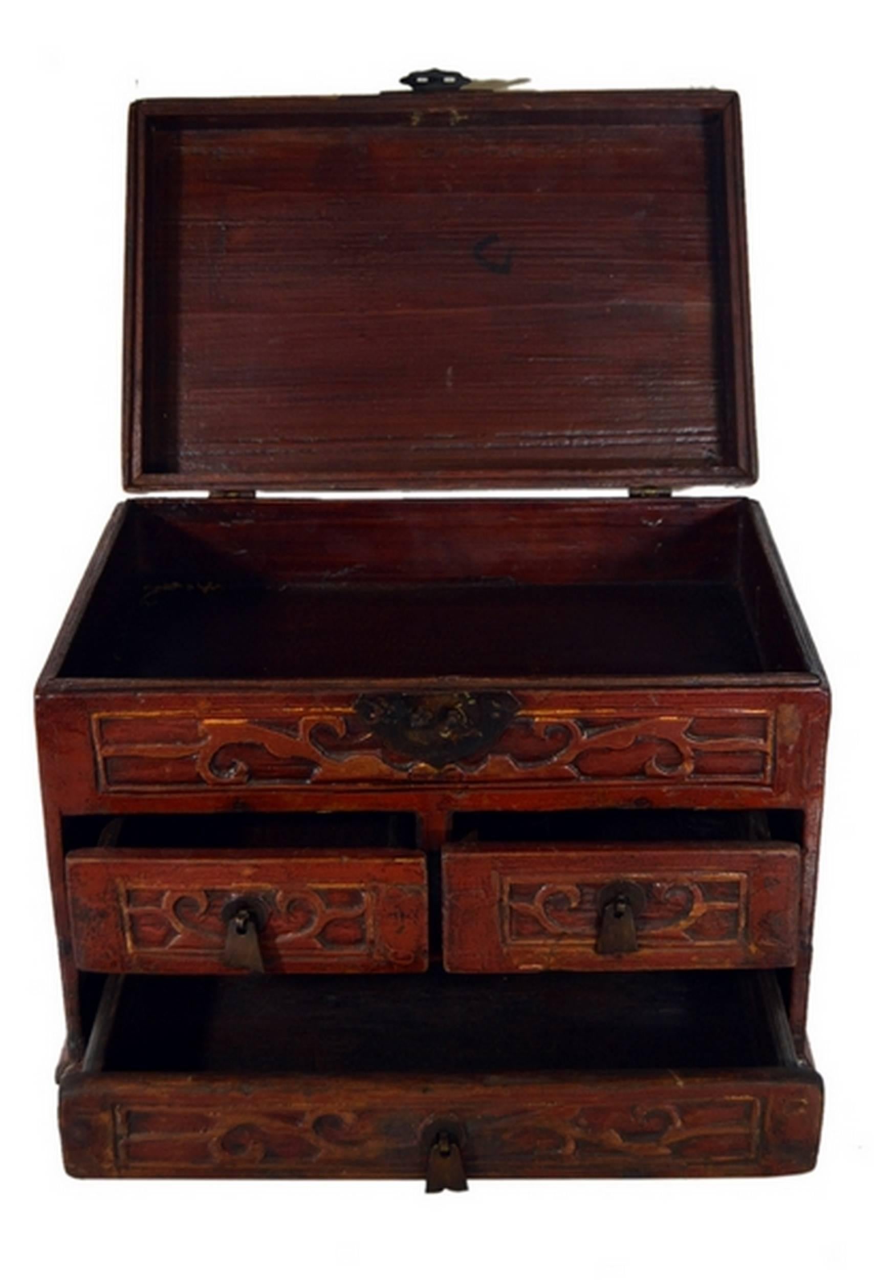 A mid-20th century Chinese jewelry box featuring carved and lacquered drawers. This small rectangular box displays a large bottom drawer and two smaller drawers with carved flat bell-shaped handles. The top opens thanks to a carved hardware lock and