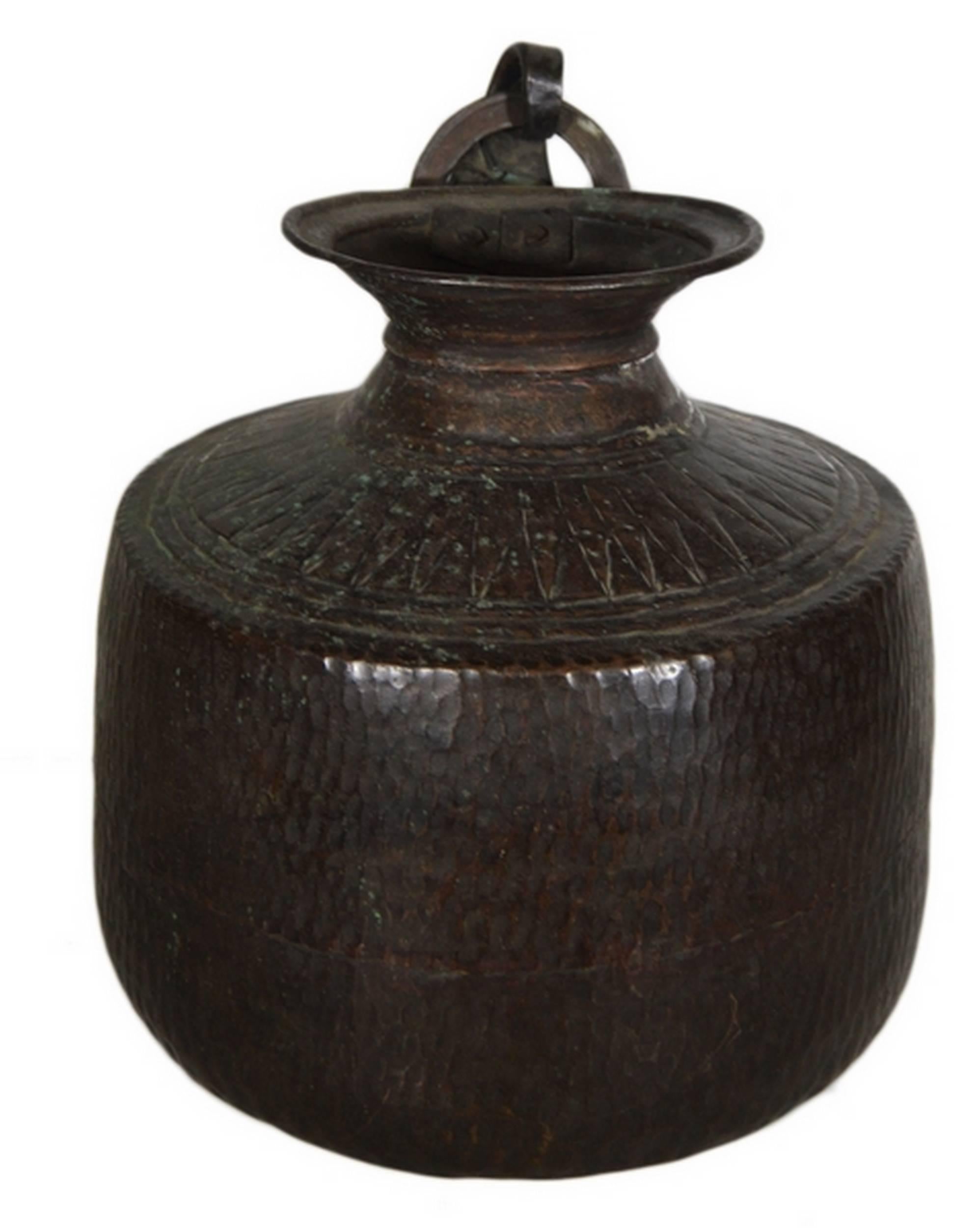 A vintage carved and hand-hammered copper jug from 1930s India. This jug displays a large belly with a round bottom and a carved top. The small flared lip features a handle with a ring which helps for hanging. This copper jug showcases its age via a