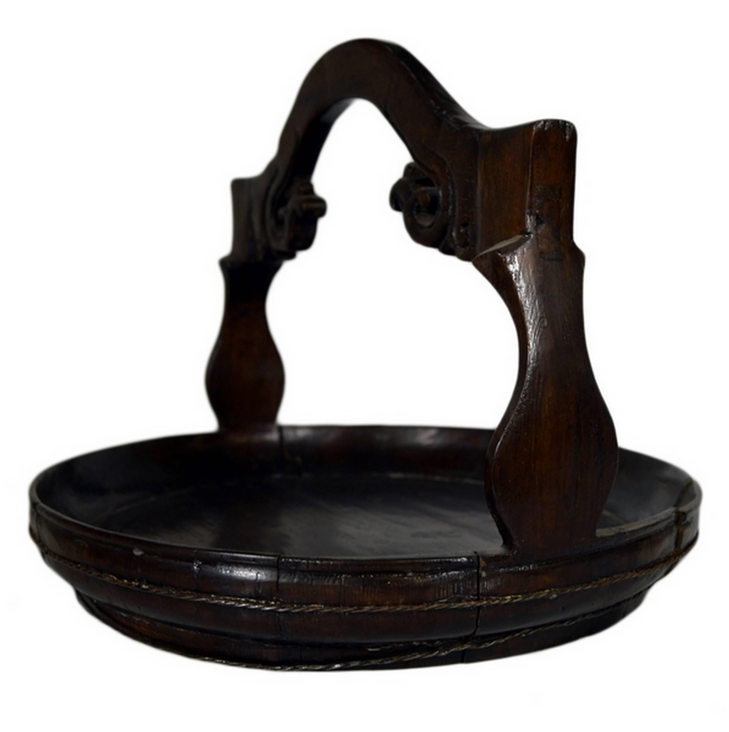 A 19th century Chinese offering basket hand-carved in dark wood. This refined basket features a circular flat base with a small raised edge, and a squat carved handle. The handle displays carved scroll details evoking foliage while two thin cords
