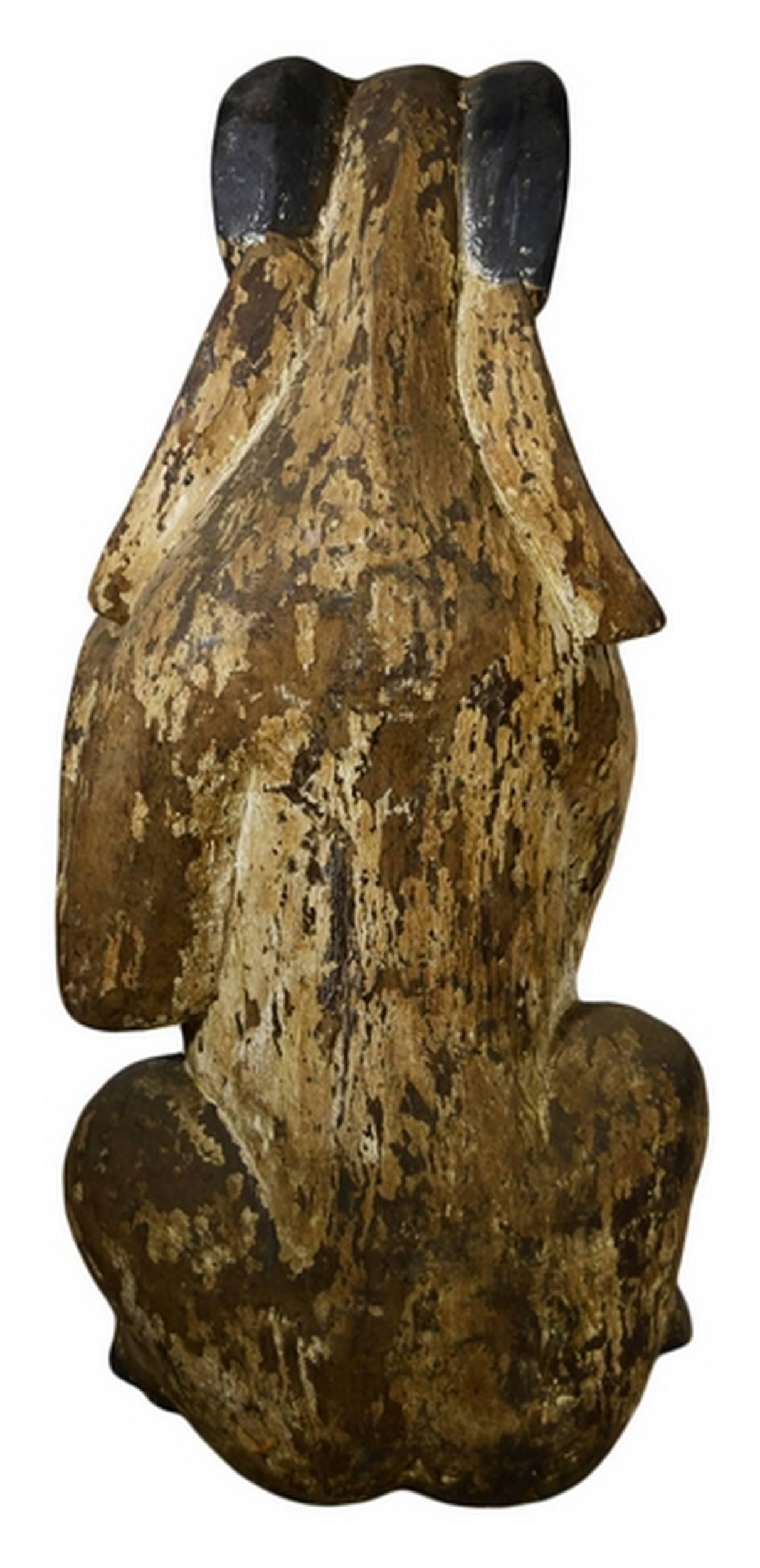 A 19th century seated goat statue hand-carved in wood from Burma. This hand-carved statue depicts a goat, seated on his hind legs with his front legs pulled up in an almost squirrel like position. The animal showcases many details, enhanced by the