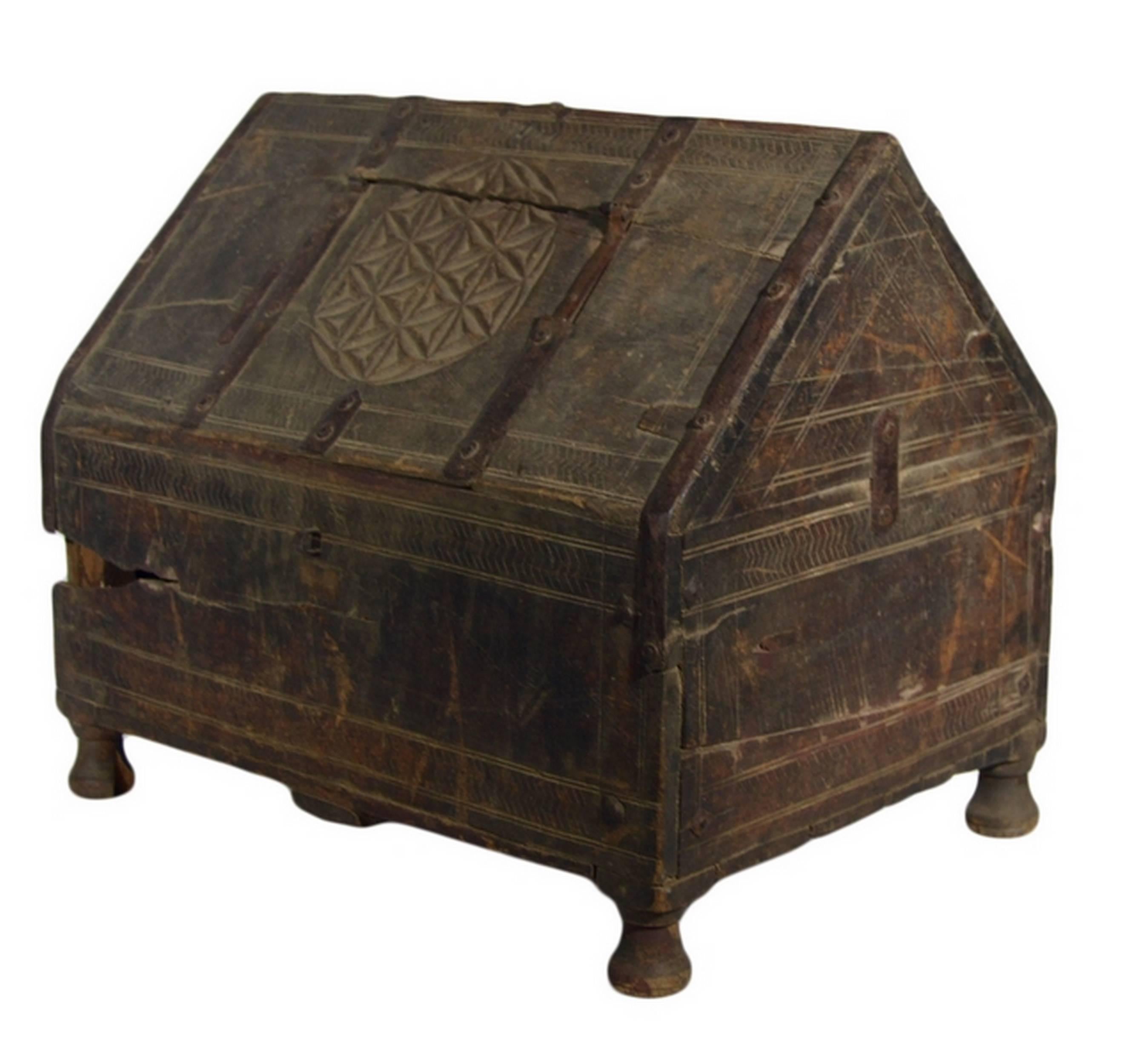 A 19th century Mughal dowry chest with carved patterns from India. This chest wooden chest with a slanted top strengthened by metal hardware reinforcements. The front displays lightly carved geometrical friezes. A large carved geometrical medallion