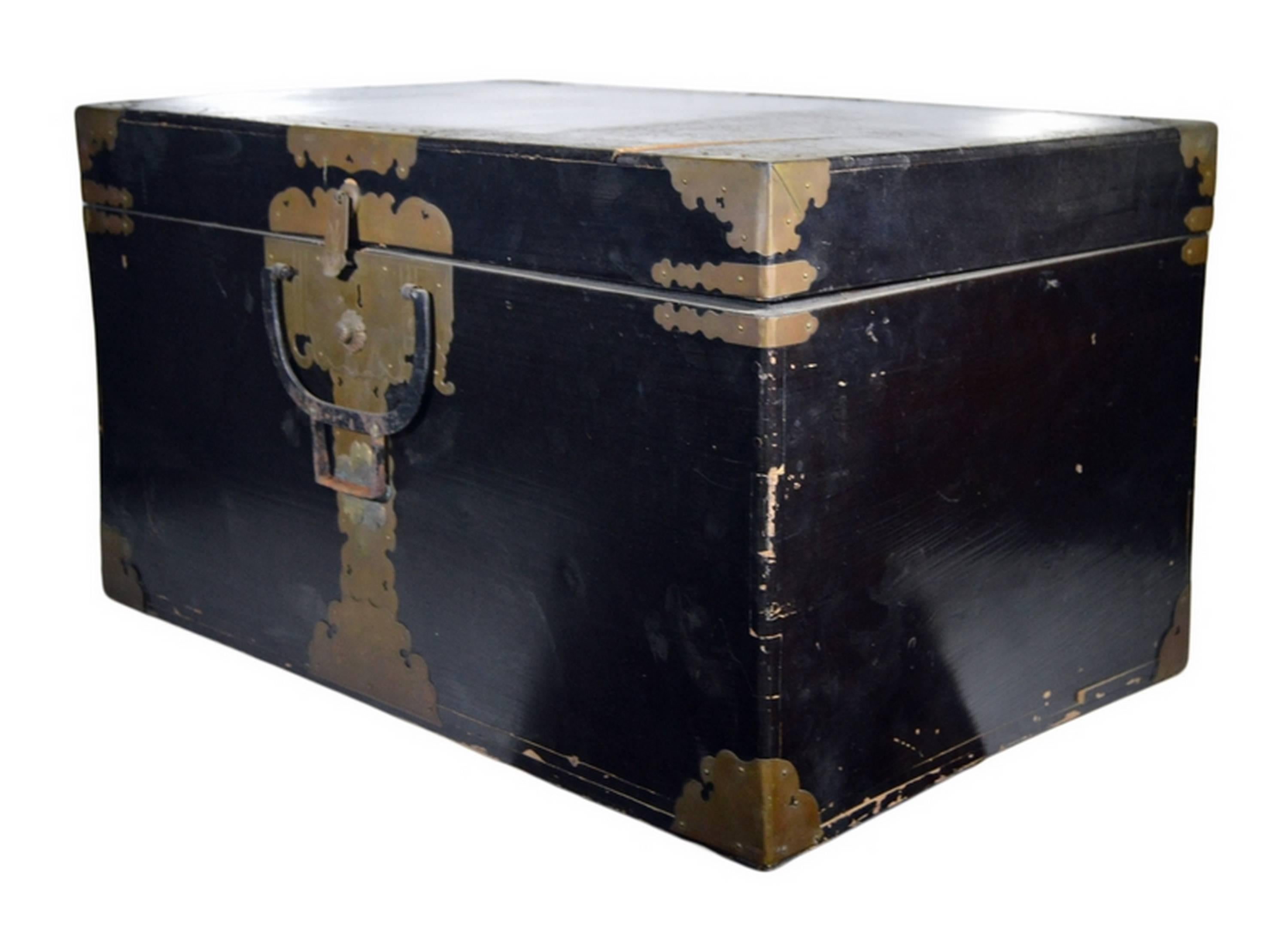 This 19th century chest was made in Japan with dark lacquered wood and brass hardware. This rectangular wooden chest is covered with an attractive dark and shiny lacquer. Carved brass hardware reinforces the corners and adorns the front center,