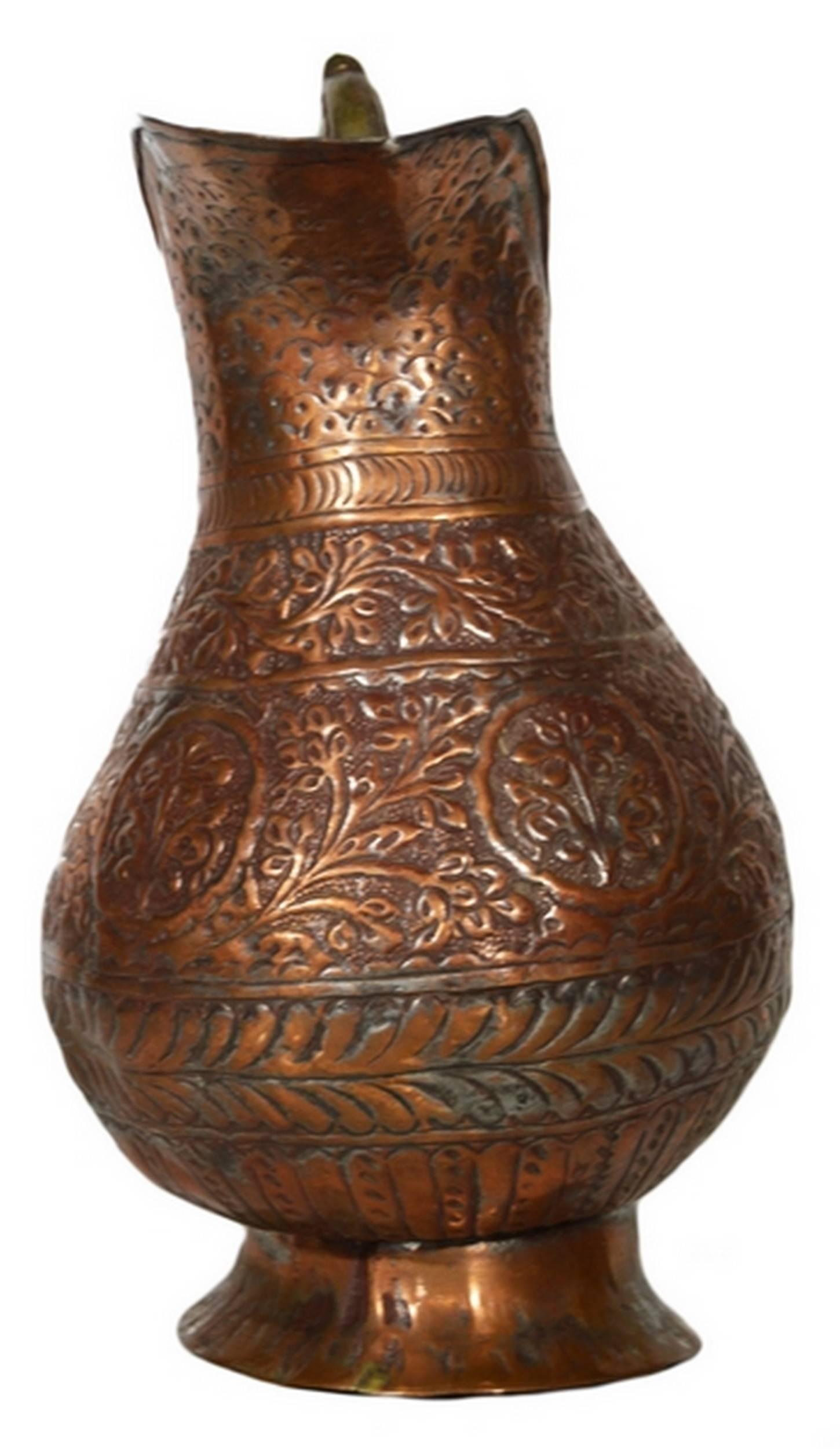 A 19th century globular pitcher hand-hammered in copper with many details from India. This pitcher adopts a globular shape with a large belly resting on a flared base. The top is narrow and features a tall spout and a thin handle. The item was