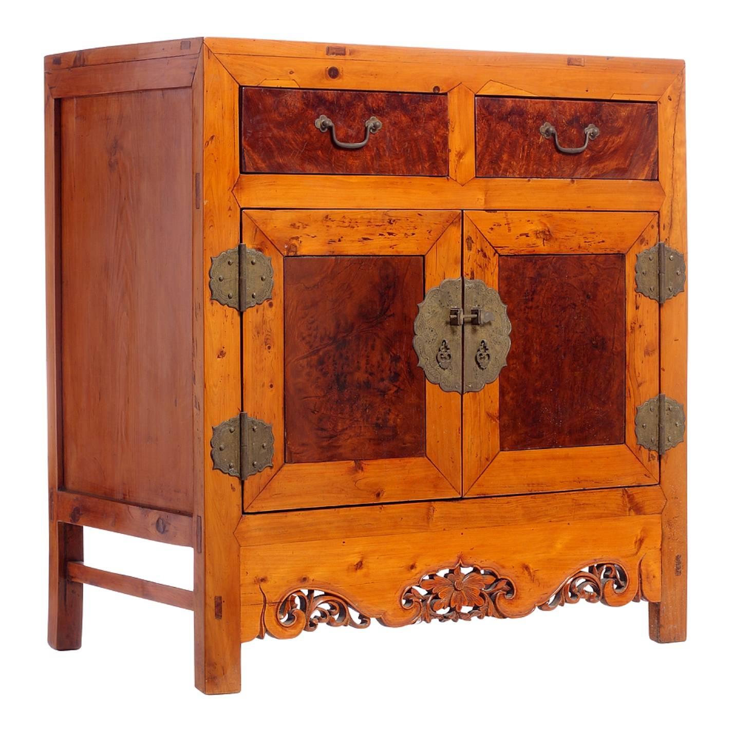 This Chinese side cabinet from the turn of the century (19th-20th century) features two drawers over two doors and is made of elm with burl wood panels on its front. The skirt is nicely adorned with pierced motifs made of a central flower and