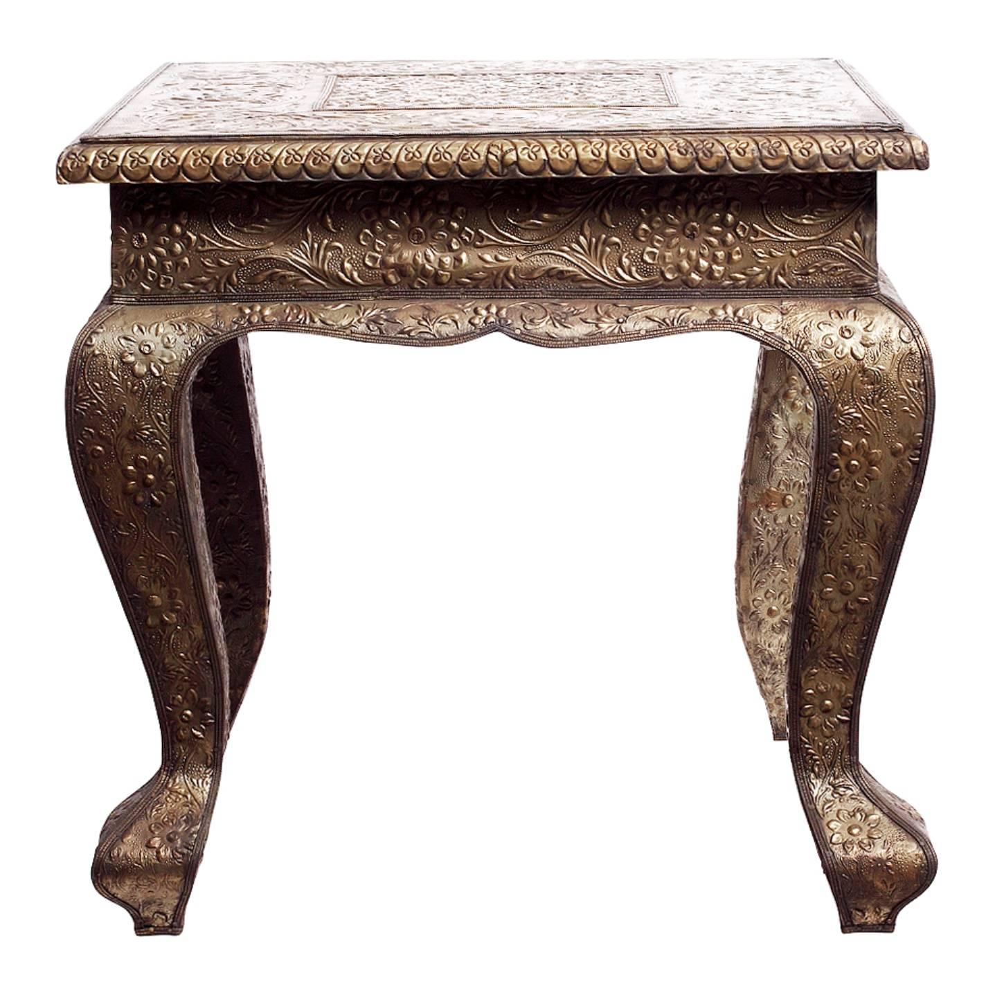 A square Indian table with flower patterns made with hammered and detailed silver. The table showcases a square top supported by four curved legs via a belt immediately below the top. The piece is made of hammered silver covered everywhere by