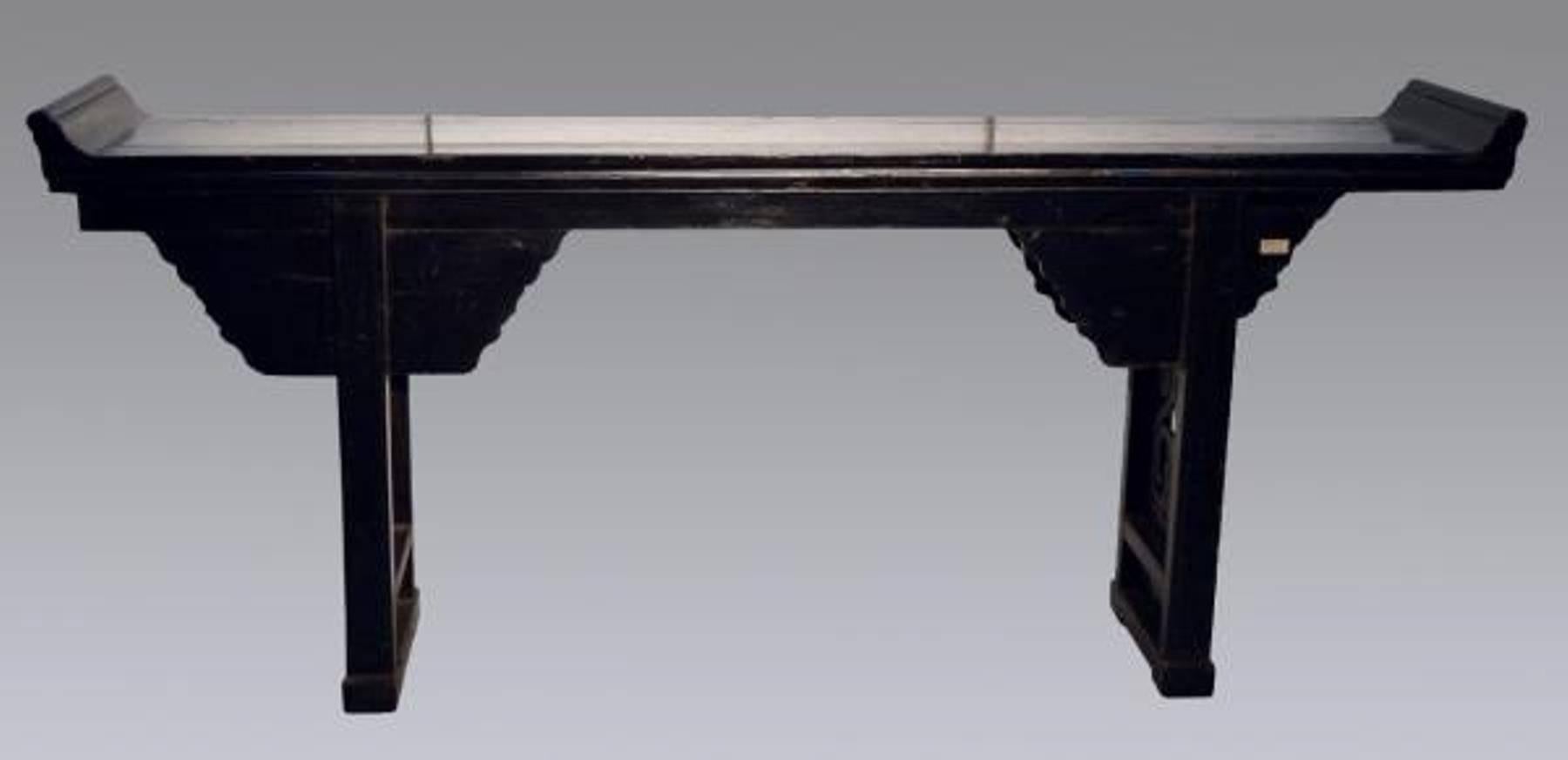 A black lacquered Chinese console table from the 19th century. This console table originally an altar table features black lacquer and a variety of carved details. This large console table showcases an elegant shape with rounded edges on the sides