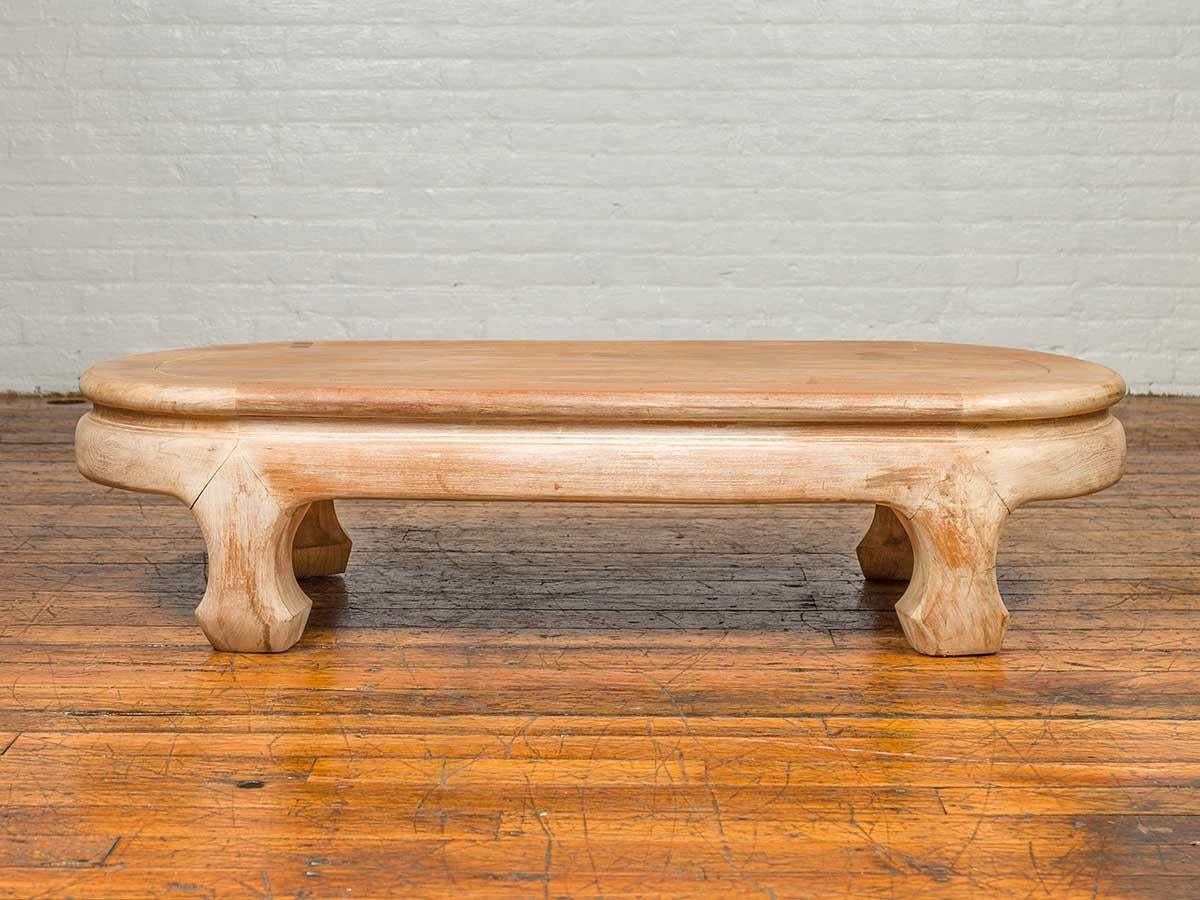 A vintage Thai teak wood oval top coffee table from the mid-20th century, with whitewash finish and chow legs. Crafted in Thailand during the mid-century period, this teak wood coffee table features an oval waisted top, sitting above a base