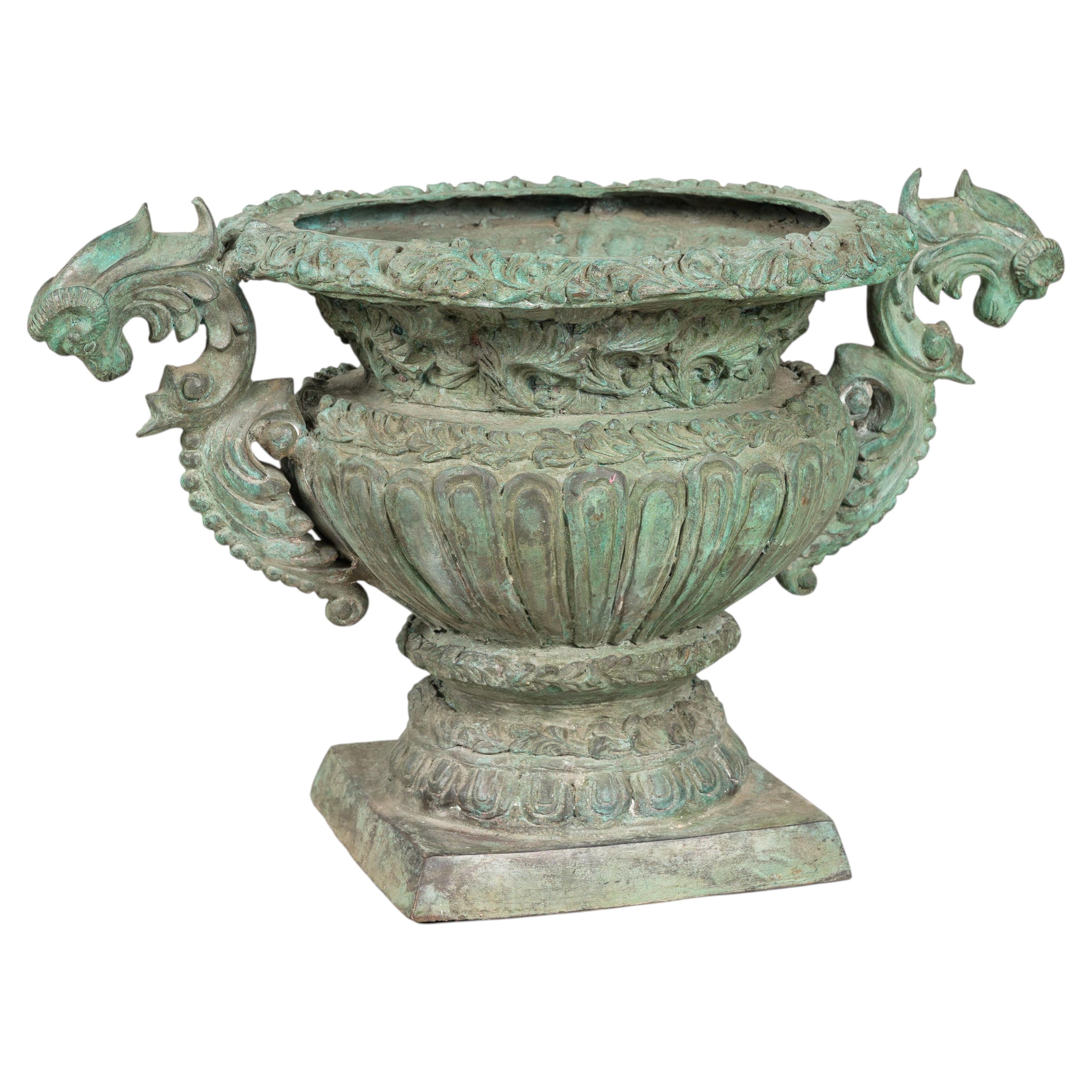 Urna de bronce de estilo grecorromano con asas en forma de cabeza de carnero y pátina verde