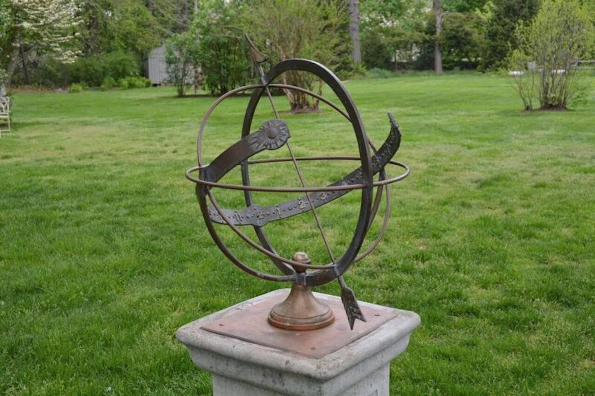 A bronze armillary sphere, with multiple celestial rings, including a numbered equatorial ring, the whole pierced by an arrow, on rising socle and integral bench, French, ca. 1950.  On an associated narrow Art Nouveau style composition stone plinth