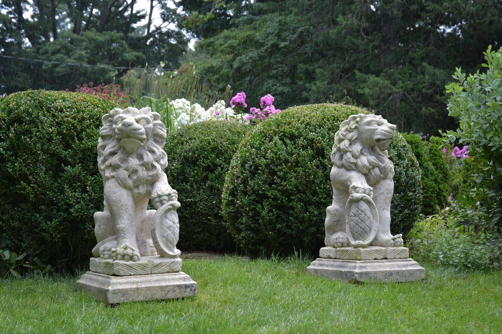A pair of carved stone gate pier seated lions, looking in opposing directions, each fully-maned beast with one paw raised on a heraldic shield, Bavaria, early 19th century. Measures: Lions 36 ins high, self-bases 5 ins high, 17.5 ins wide, 21 ins