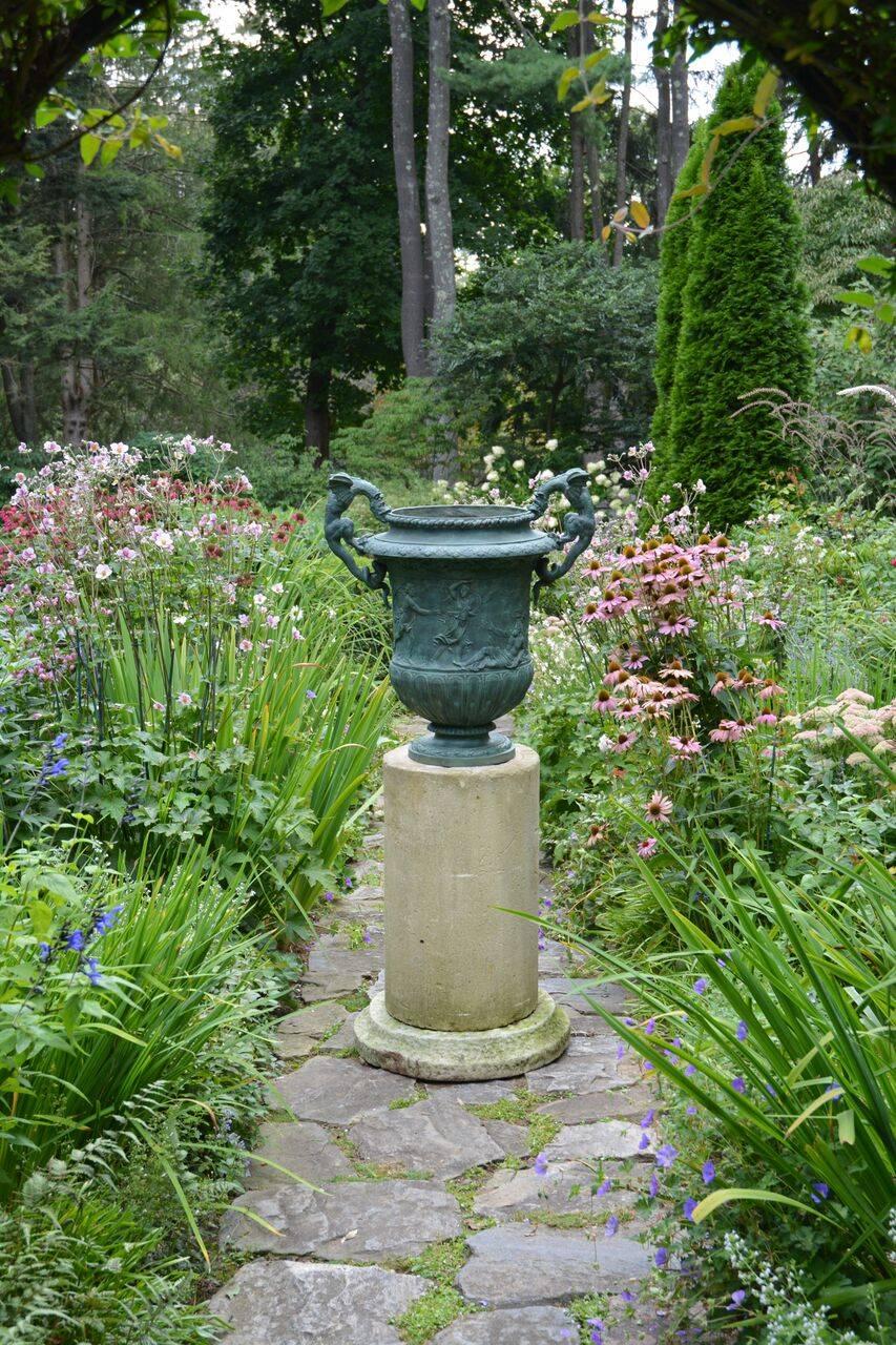 A large single cast-iron urn with dragon handles, the body of the urn ornamented with classical scenes, possibly French, circa 1900. Measures: Urn 30 ins. high, 28 ins. overall width, 14.5 ins. diameter of opening. On an associated columnar carved