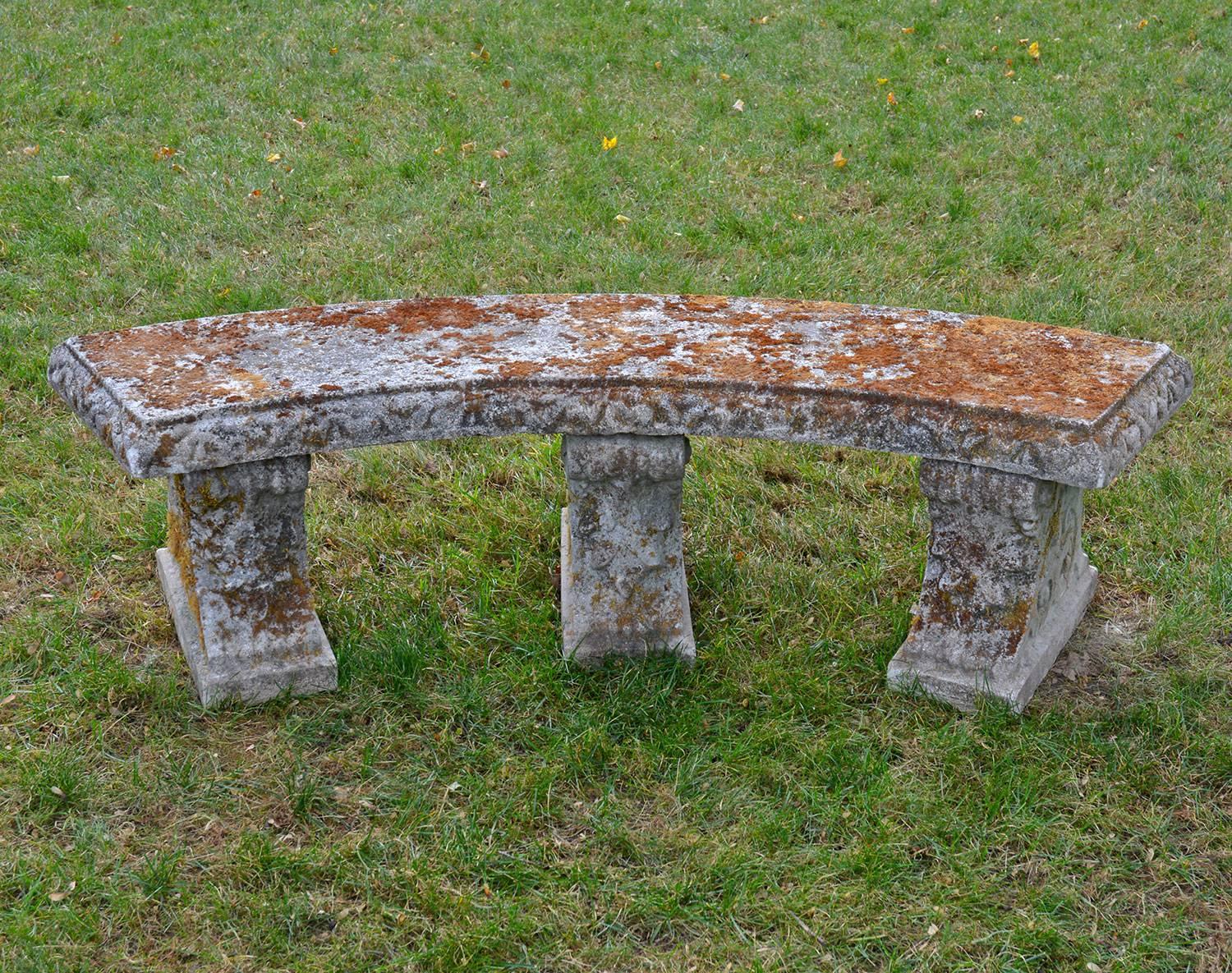 A curved composition stone bench with three scroll supports, English, circa 1950.  17.5 ins. high, 64 ins. wide, 22 ins. overall depth, top surface 17.25 ins. deep. 