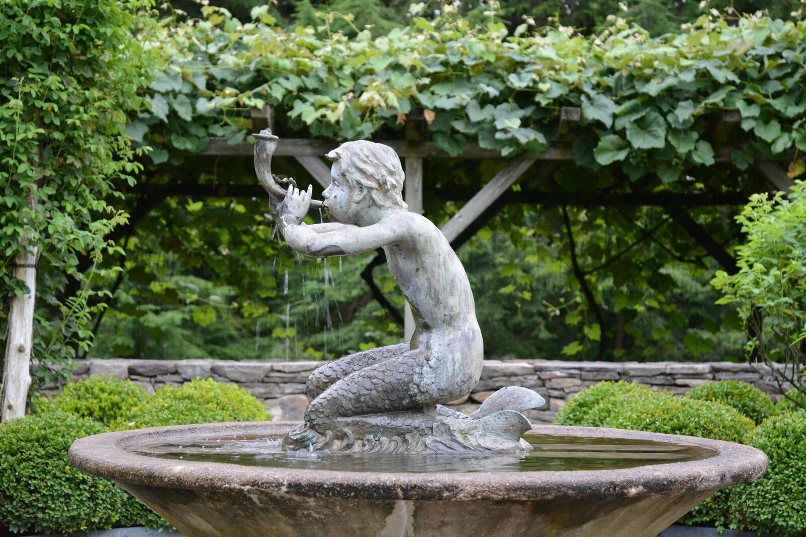 An unusual white metal fountain figure of a seated merboy blowing a Horn, verdigris patination, piped for water. American, circa 1960.