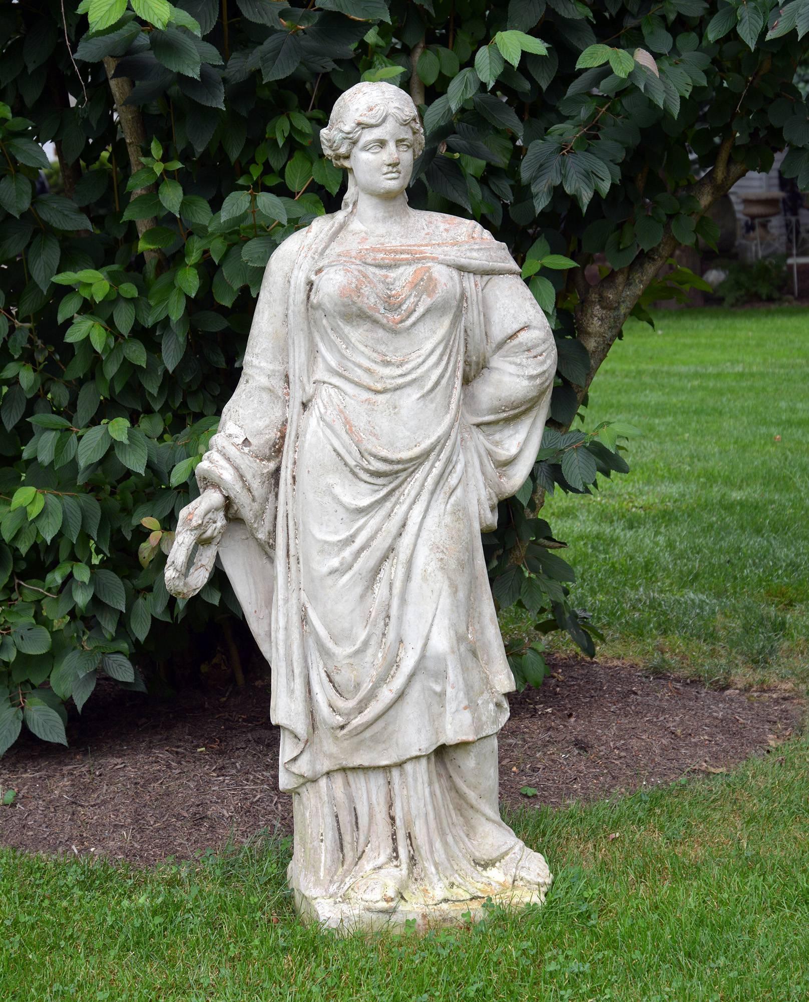 A painted terra cotta female figure in heavily draped classical dress, barefoot and holding a laurel wreath in outstretched proper right hand, possibly representing Chloris or Flora (Roman).