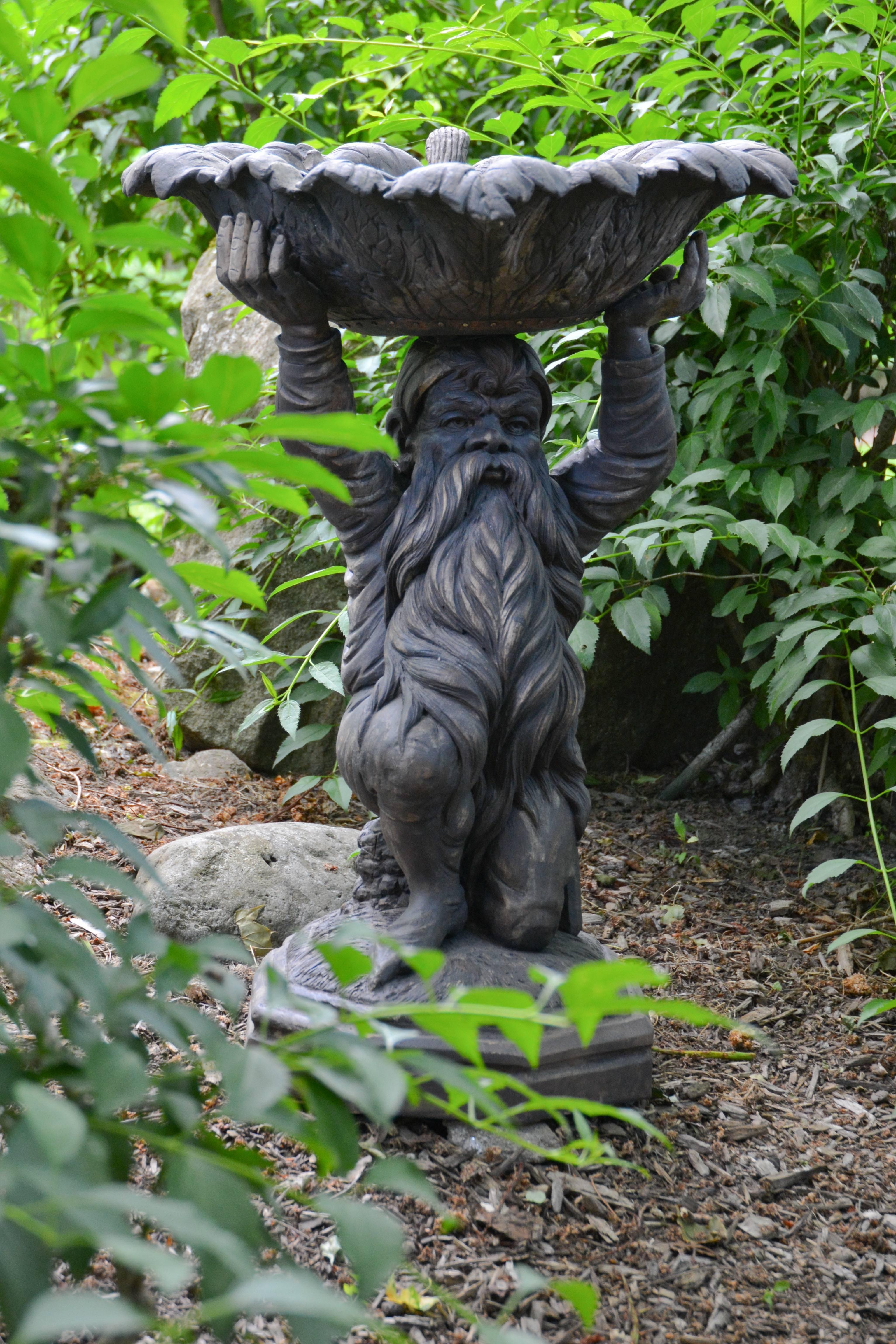 An unusual carved wooden birdbath in the form of a kneeling bearded dwarf, holding a leafy basin on his head, the basin lined with lead sheeting, Scottish (by repute), circa 1880.