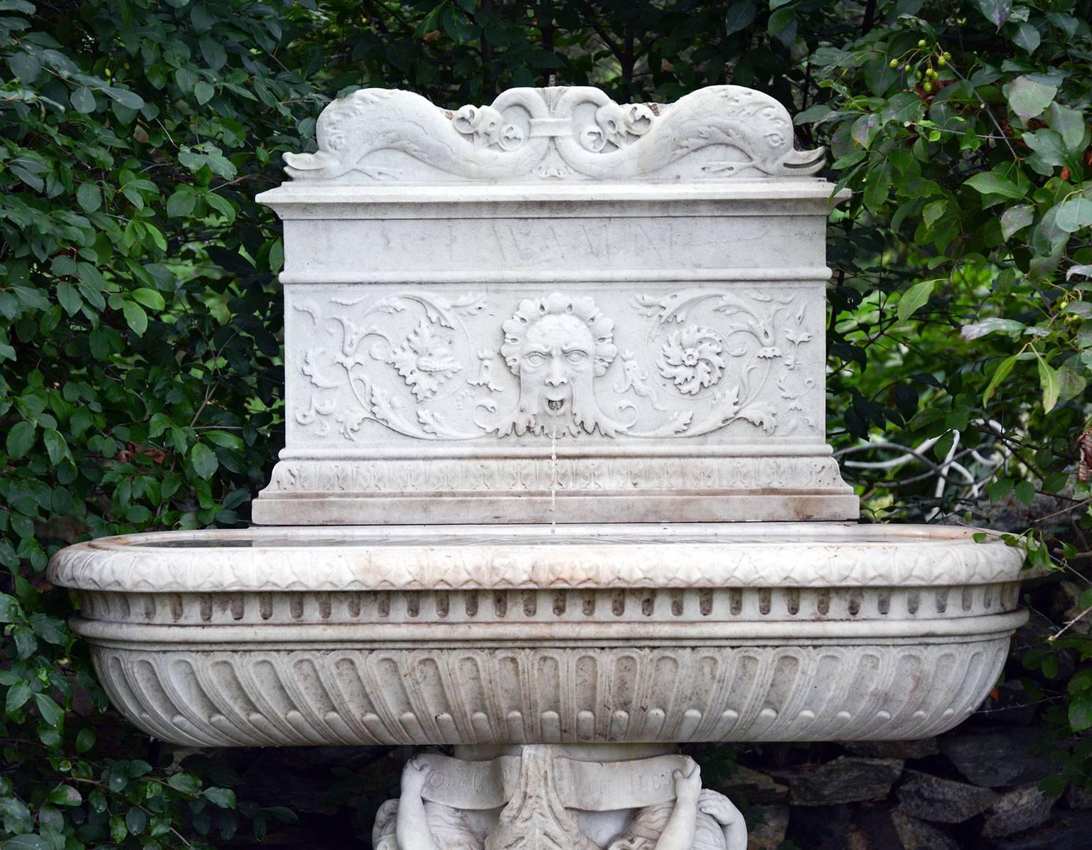 An exceptional carved marble lavabo, or wall fountain, comprised of three pieces, the backplate with lapidary script reading “LAVAMINI,” meaning “to wash,” ornamented with stylized dolphins, floral rinceaux, and a central “Green Man” mask piped for