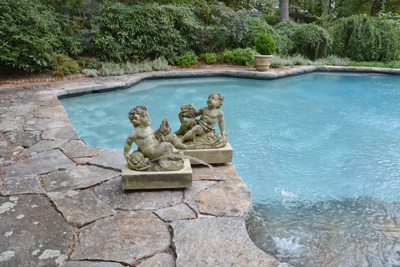 A pair of carved Vicenza stone fountainheads, each with curly haired cherub reclining on dolphin, one fountainhead piped in two places, the other piped in one, on rectangular bases, Italian, circa 1920. Measure: 28 ins high including base, bases 25