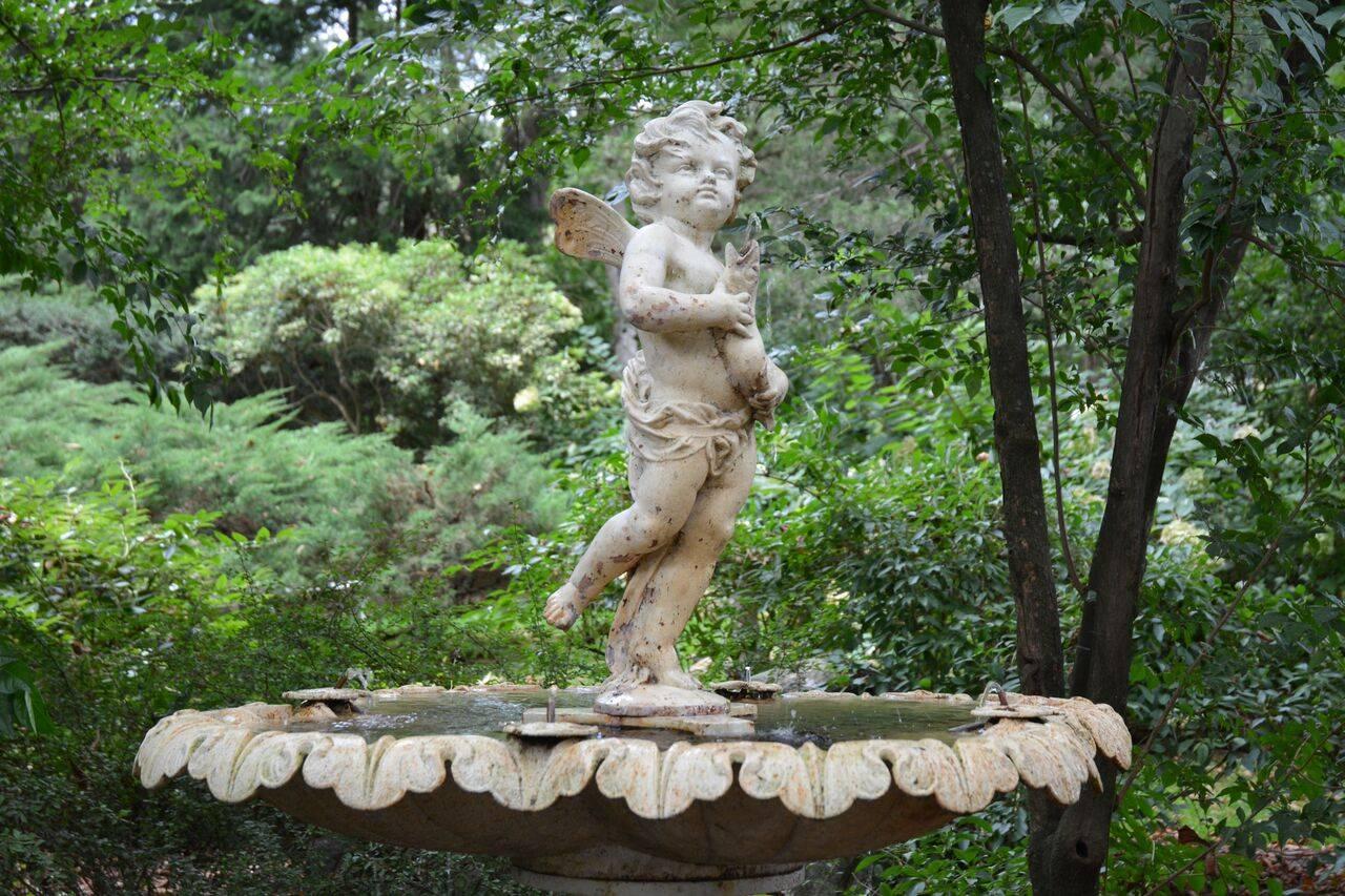 A cast-iron fountain figure of a winged cherub with upturned countenance and windblown hair, standing on his proper left leg, with right leg swept back, and holding a fish in his hands, the fish plumbed for water, French, ca. 1870, the base marked