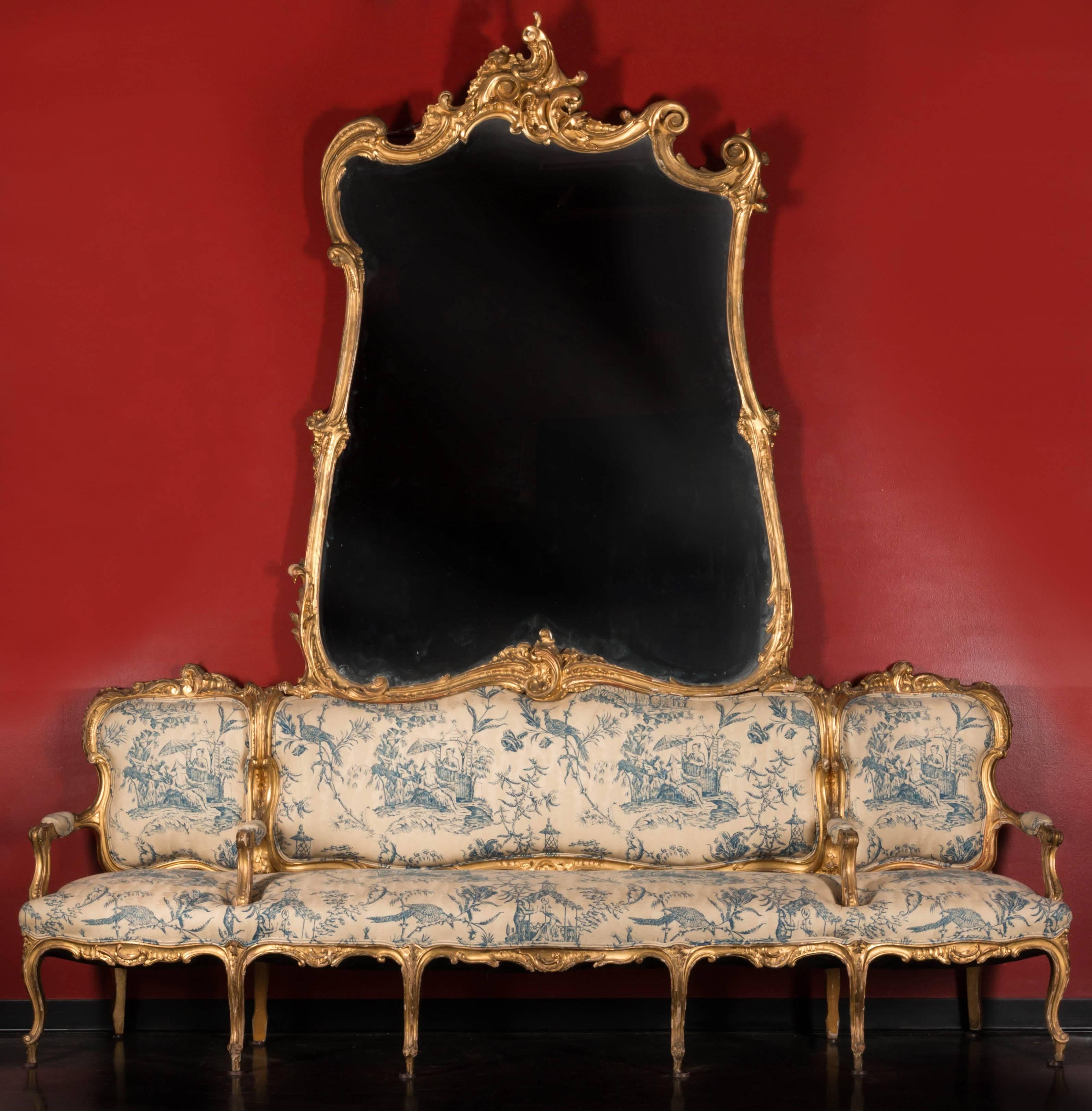 A large-scale German Louis XV giltwood "Canape de L'Amitie" with mirror. 

Comprising an irregular cartouche-shaped plate having an arched crest of C-scrolled rocaille above similarly detailed sides and rail which centres a similar