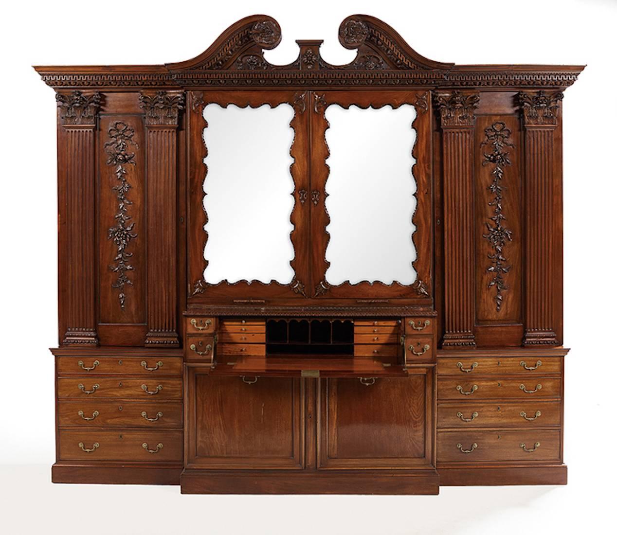 George II Palladian  mahogany breakfront bookcase, 18th century 

The broken swan's-neck pediment with gadroon- and dentil-carved bands terminating in a foliate roundel, above a like-carved frieze over two central doors, each inset with a shaped