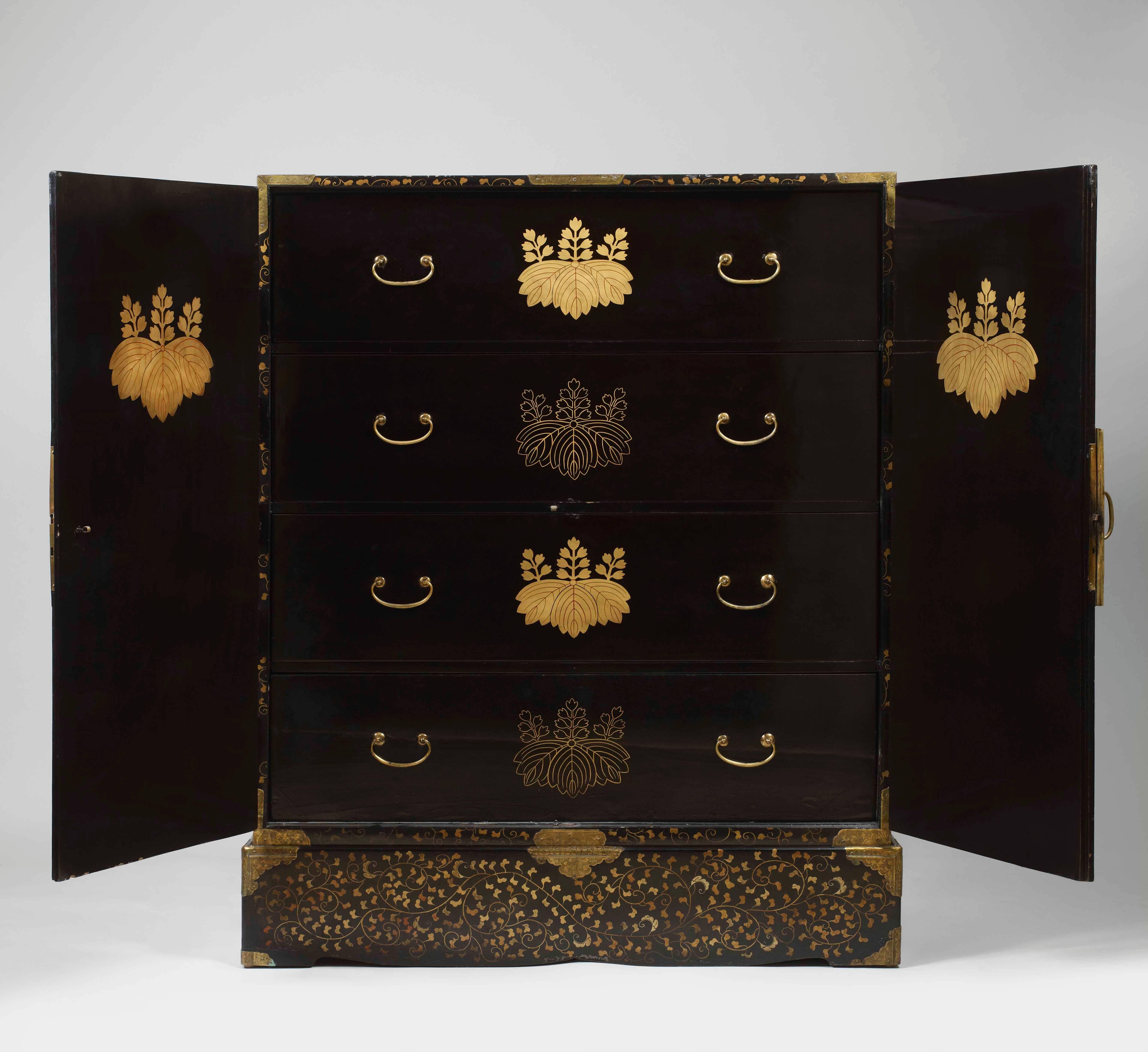 A Chinese export parcel-gilt black lacquer cabinet on stand lacquered to imitate Japanese lacquer, the pair of doors emblazoned with the crest of Mikado go-shichi no oni-kiri or Paulownia flower, the two doors centered by a brass lock plate opening