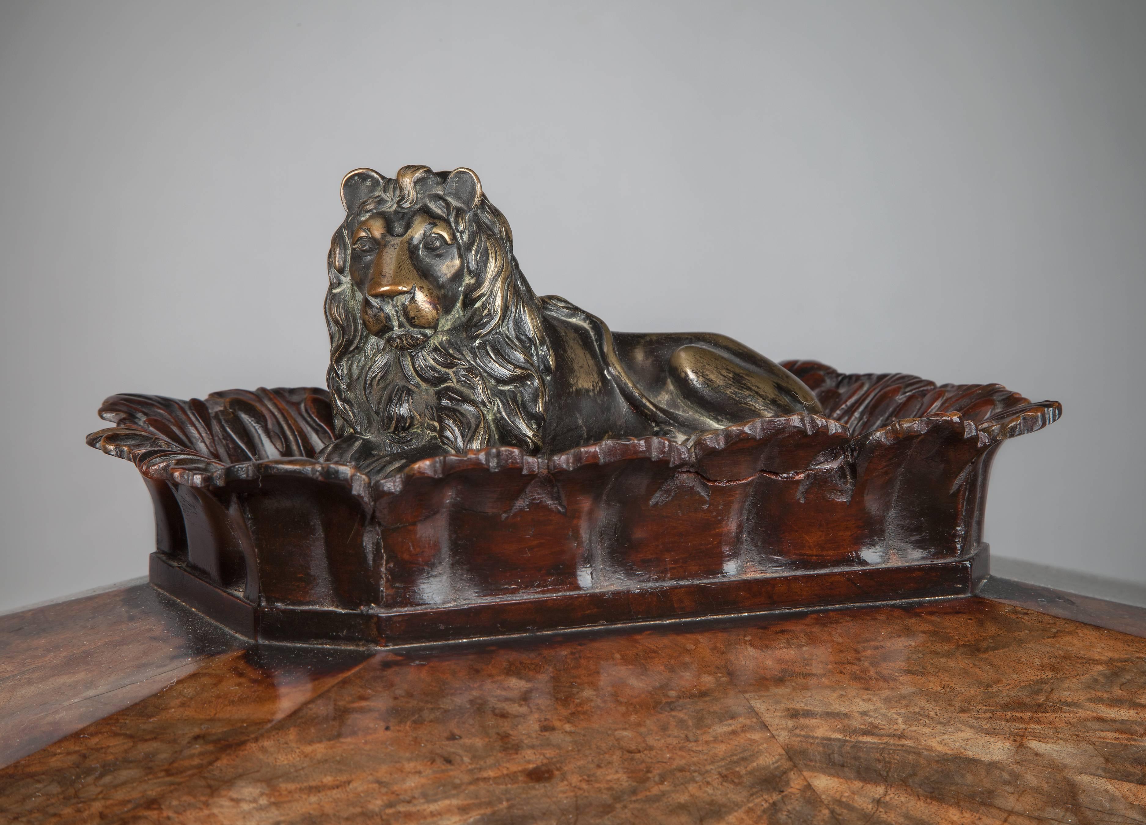 An early 19th century Regency mahogany sarcophagus wine cooler, the pitched lid adorned with a recumbent bronze lion framed with acanthus leaves, above a panelled base with re-entrant mouldings. The frieze decorated with circular bronze paterae